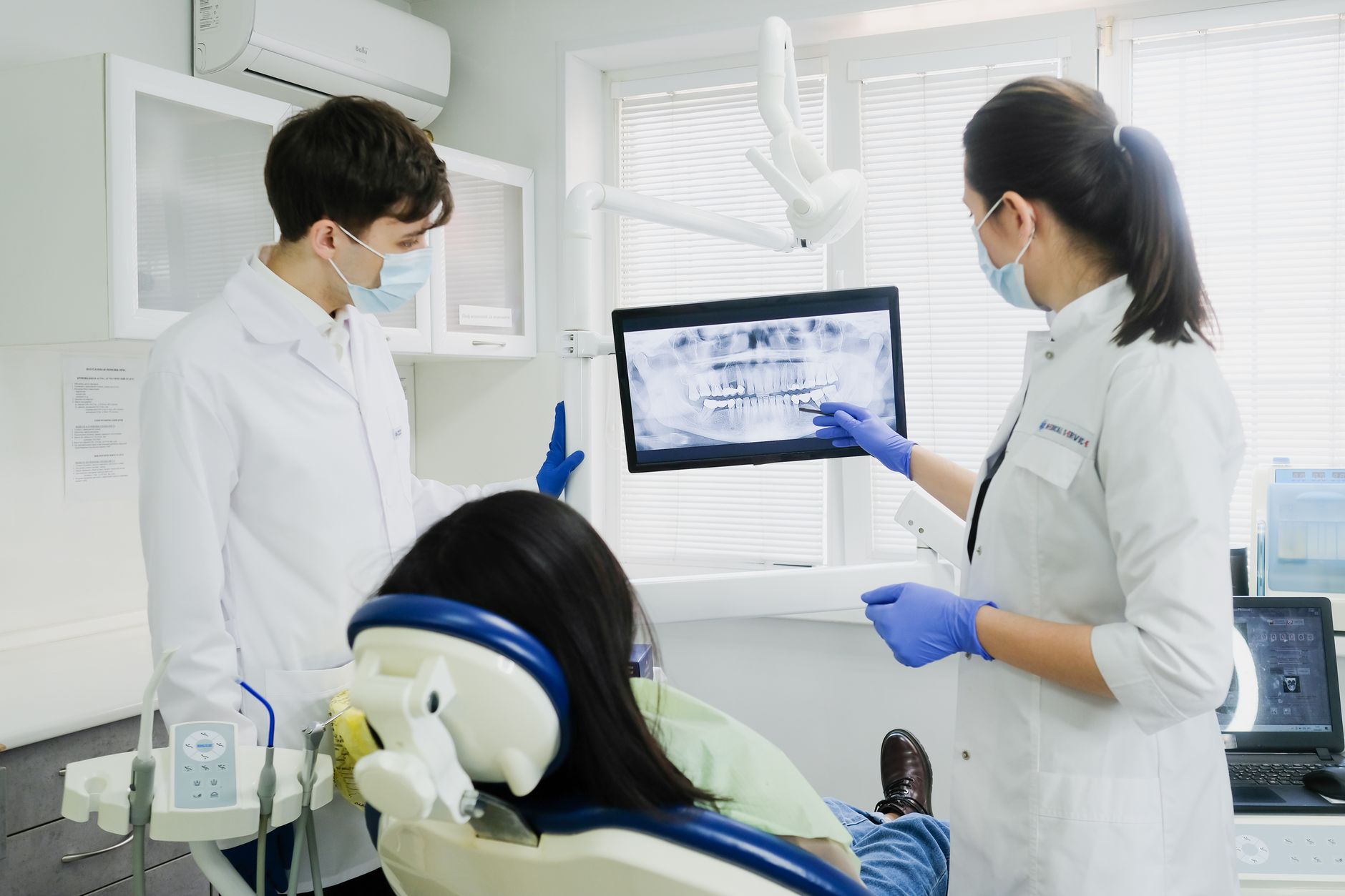 Dentists reviewing X-ray on screen with patient in dental chair.