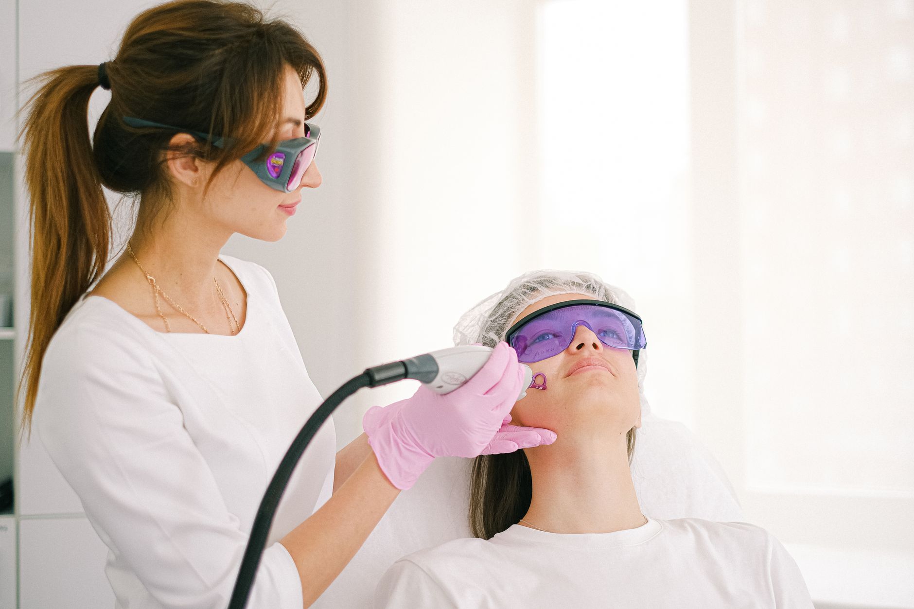 Aesthetician using a laser device for skin resurfacing on a patient's face.