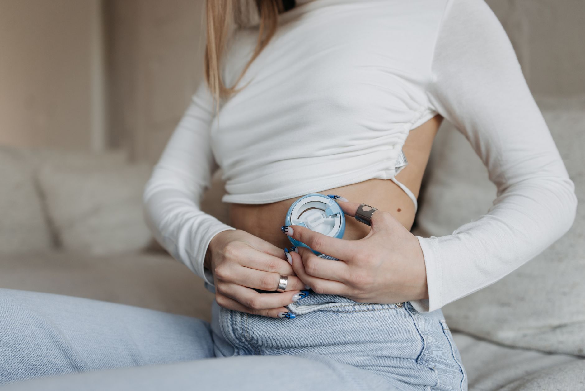 A woman adjusts her continuous glucose monitoring device while sitting on a sofa, focusing on insulin therapy.