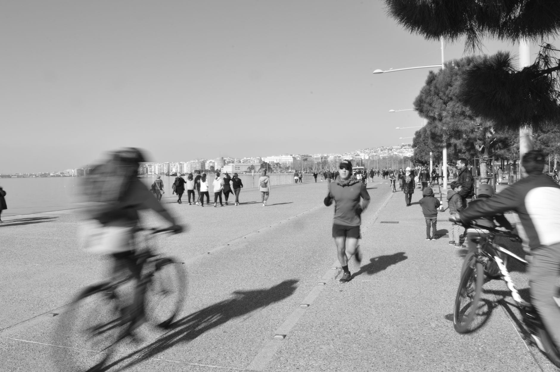 A busy promenade in Thessaloniki with walkers, cyclists, and joggers enjoying outdoor activities.