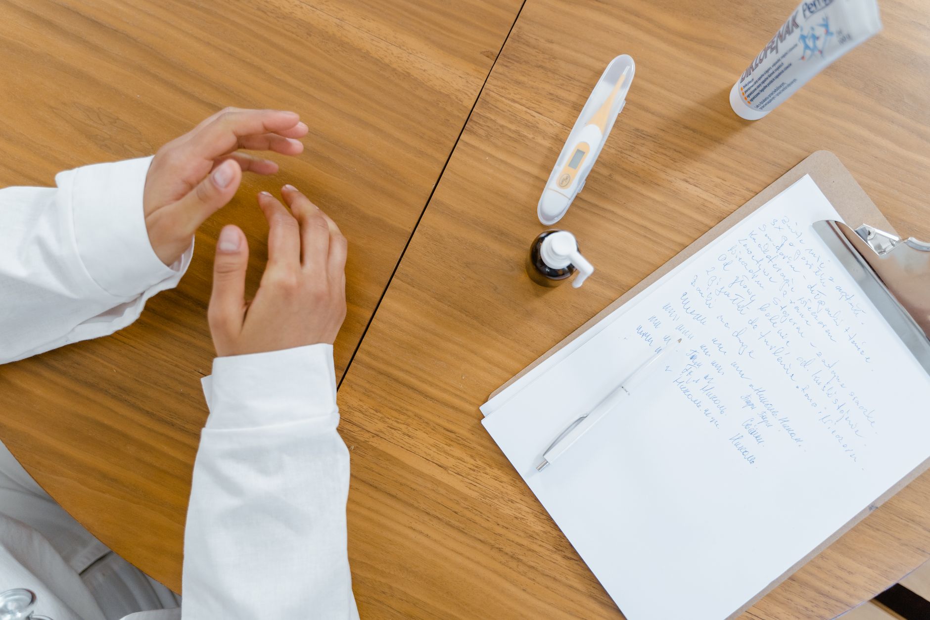 A coordinator's hands over a wooden table with a thermometer, medicine, and dialysis records.
