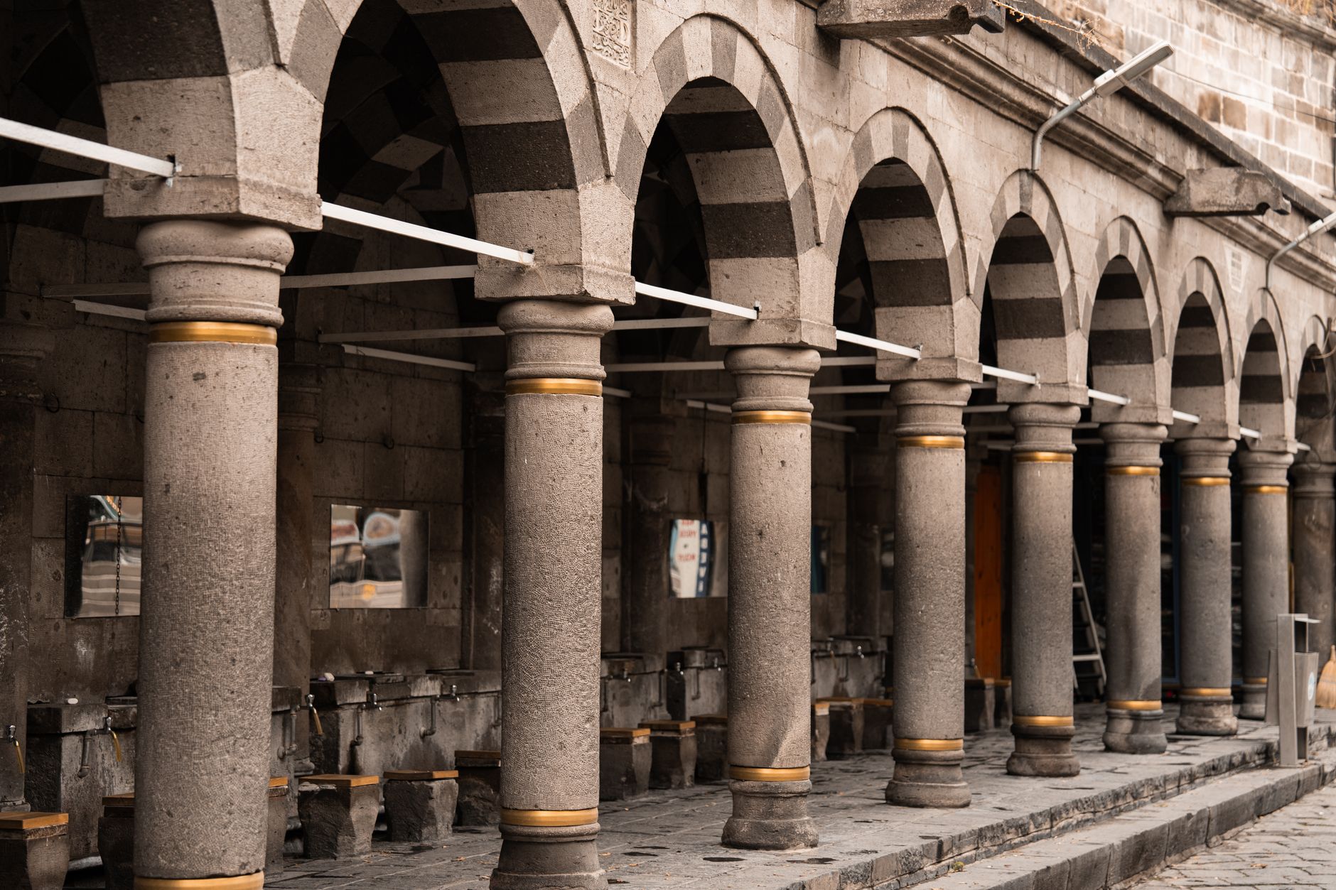 View of arched stone columns and benches in a historic mosque courtyard.