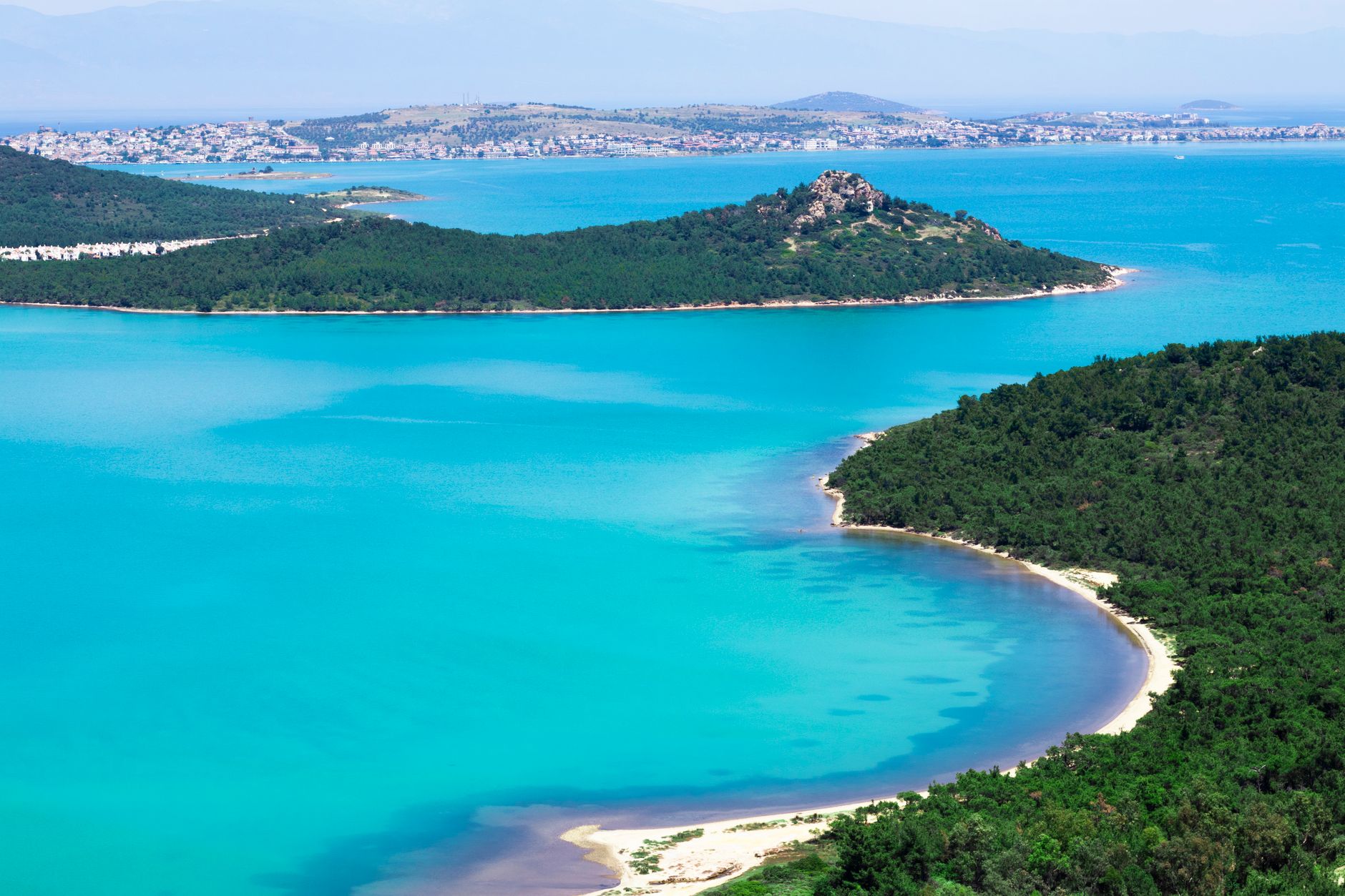 A picturesque view of a secluded sandy cove surrounded by lush greenery and turquoise waters.