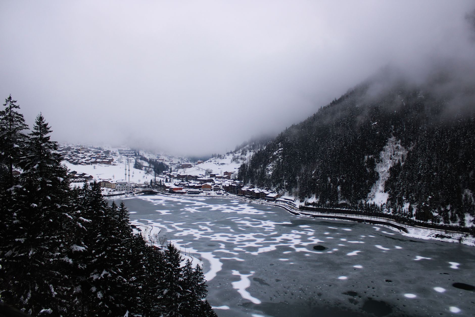 Snowy Uzungöl Lake surrounded by misty mountains and pine trees.