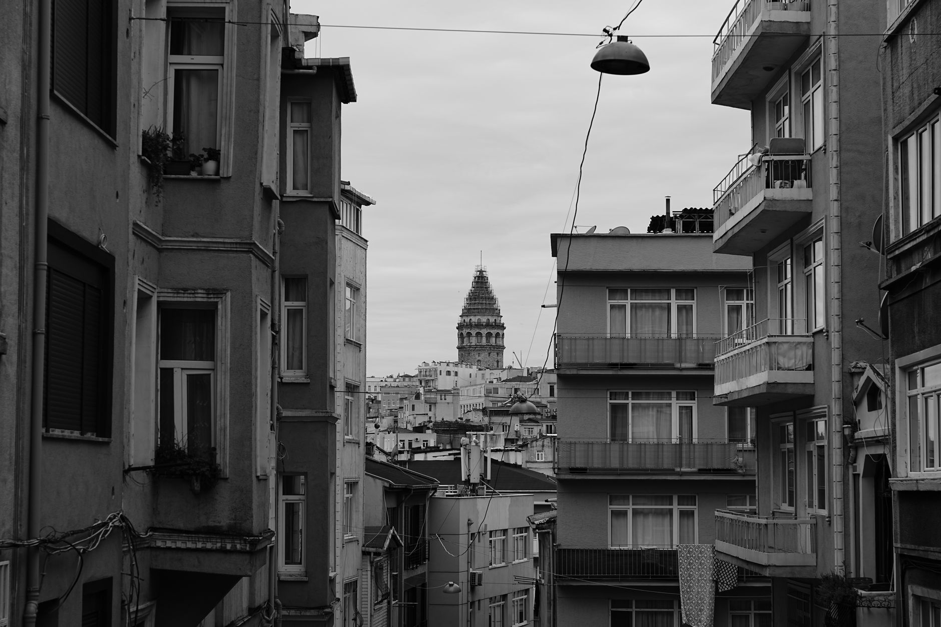 Black and white photo of Istanbul street with close buildings and Galata Tower in the background.