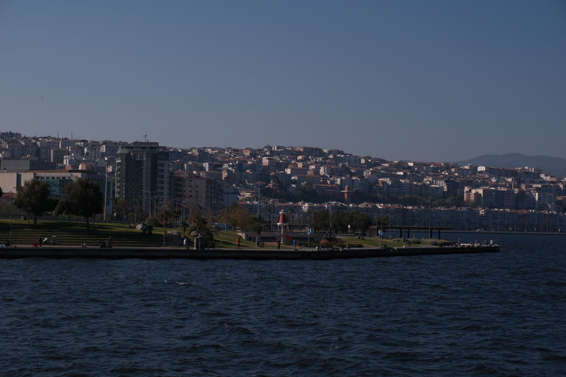 A view of Izmir's coastline and cityscape, with a serene seaside promenade and gentle waves.