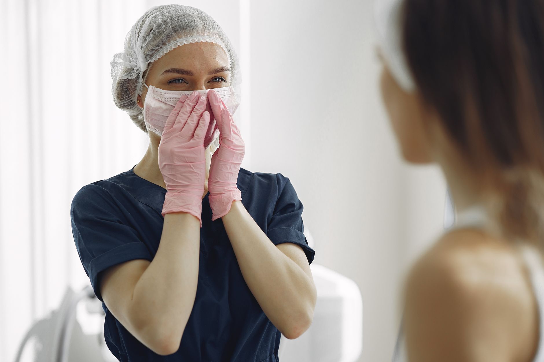 A nurse in scrubs and gloves smiles at a patient post-blepharoplasty.