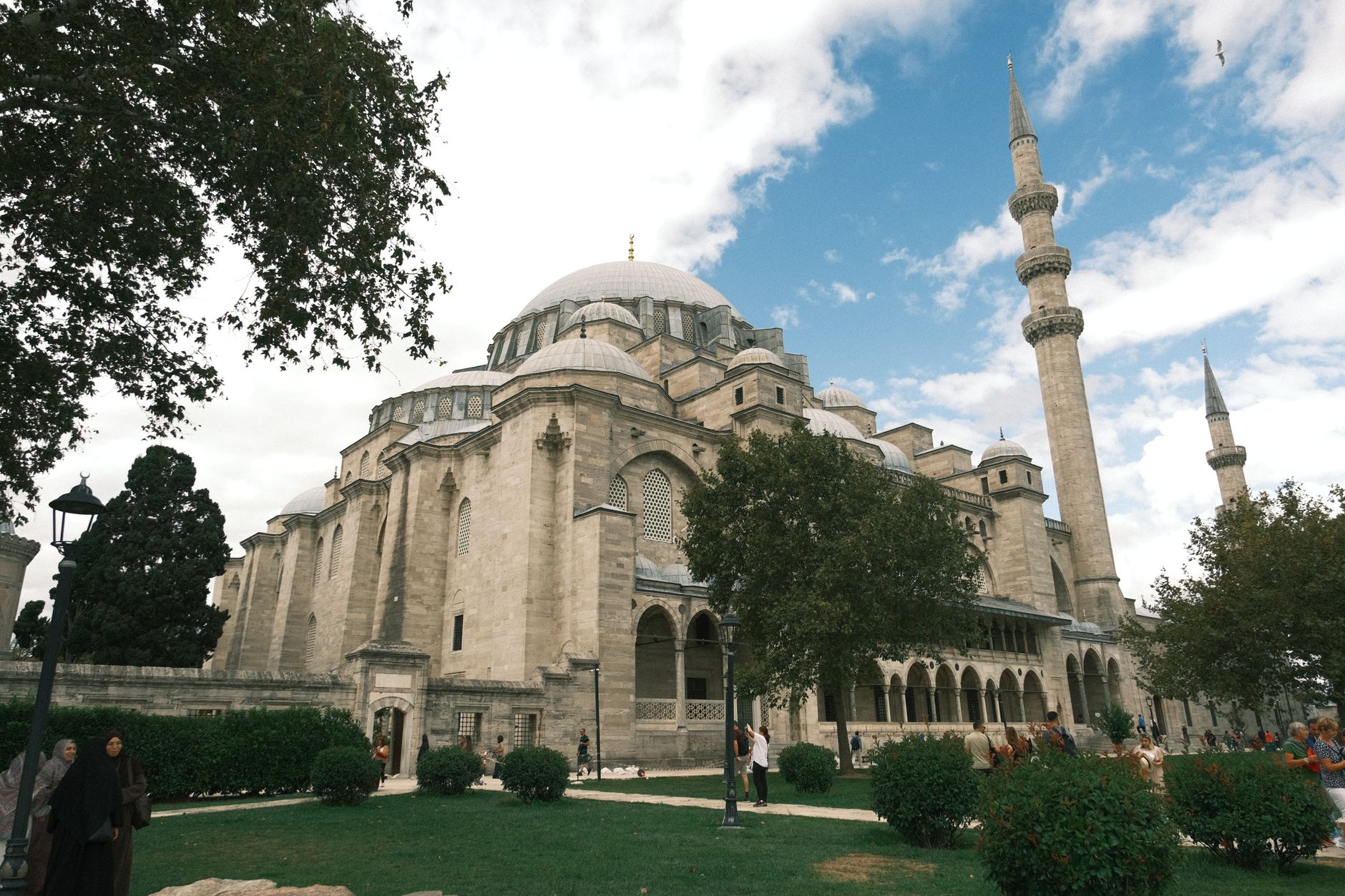A serene view of a mosque in Istanbul, featuring lush greenery and people in a courtyard.