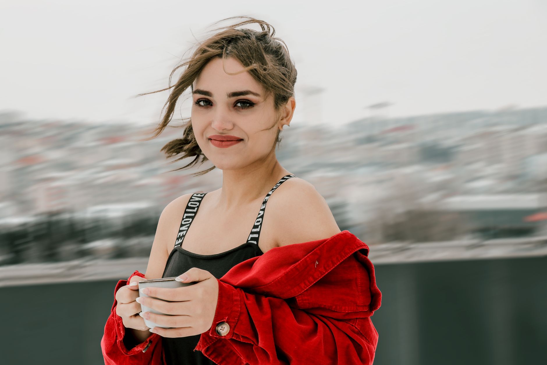 A woman with restored natural hair smiles while holding a mug, walking in Istanbul.
