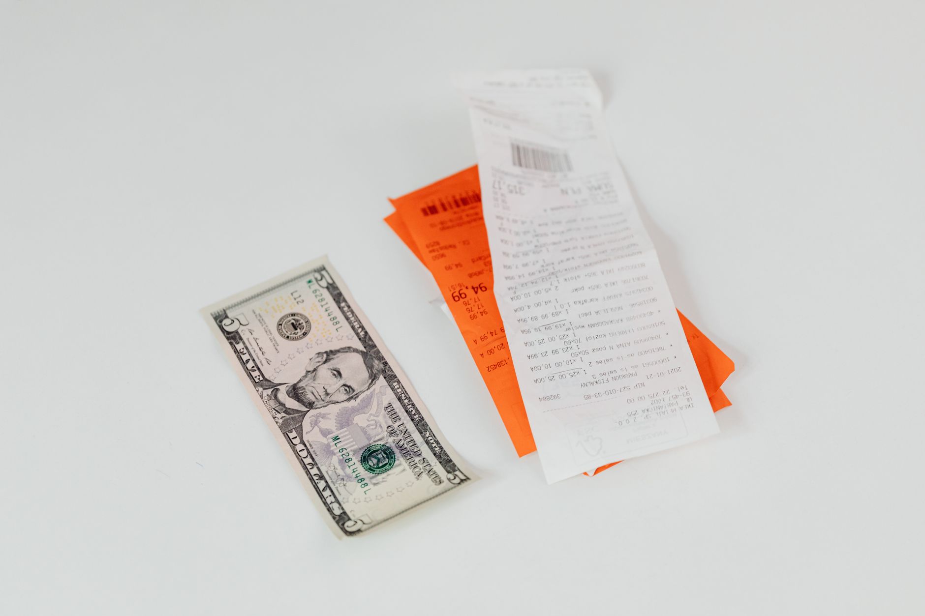 Close-up of a $5 bill next to hospital receipts and invoices on a white surface.