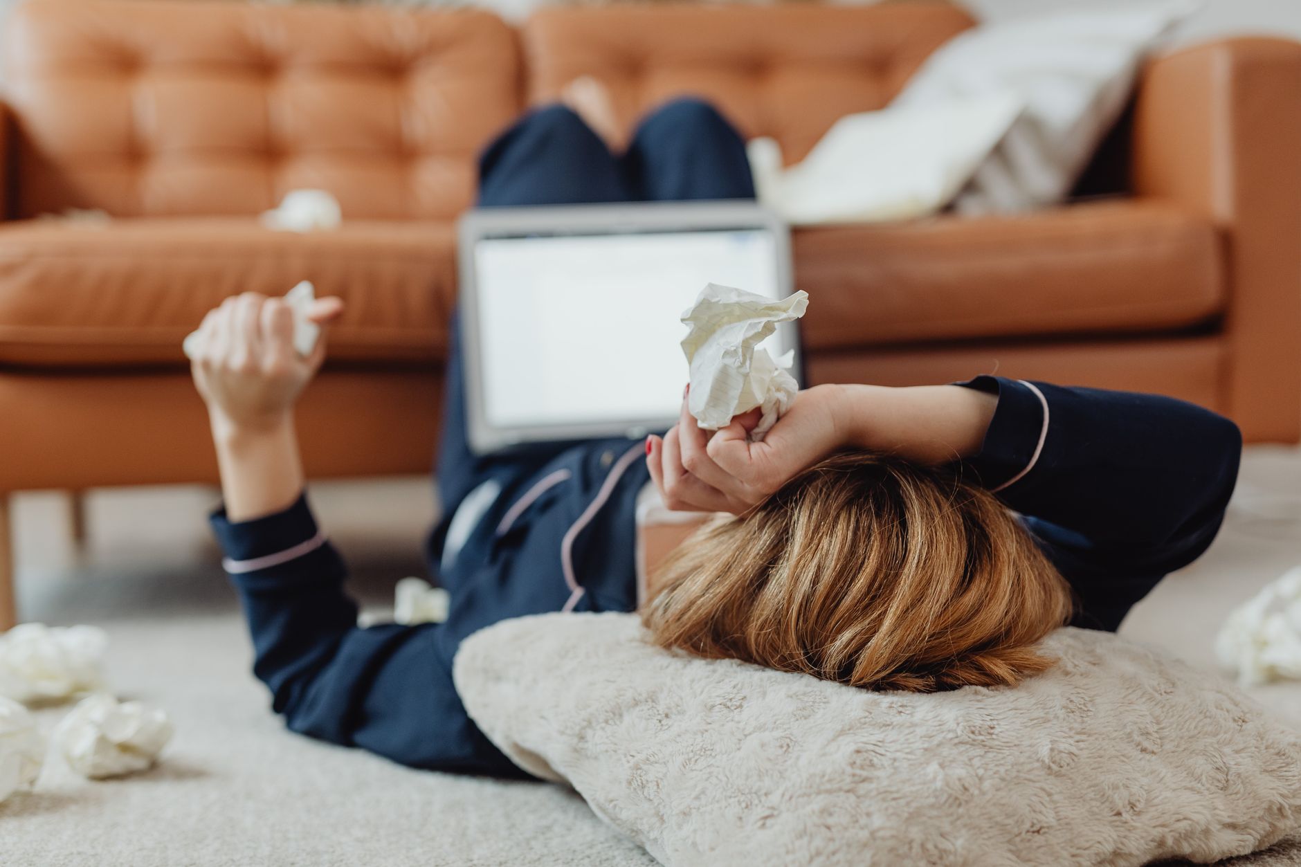 Stressed employee lying on floor with tissues, laptop nearby.