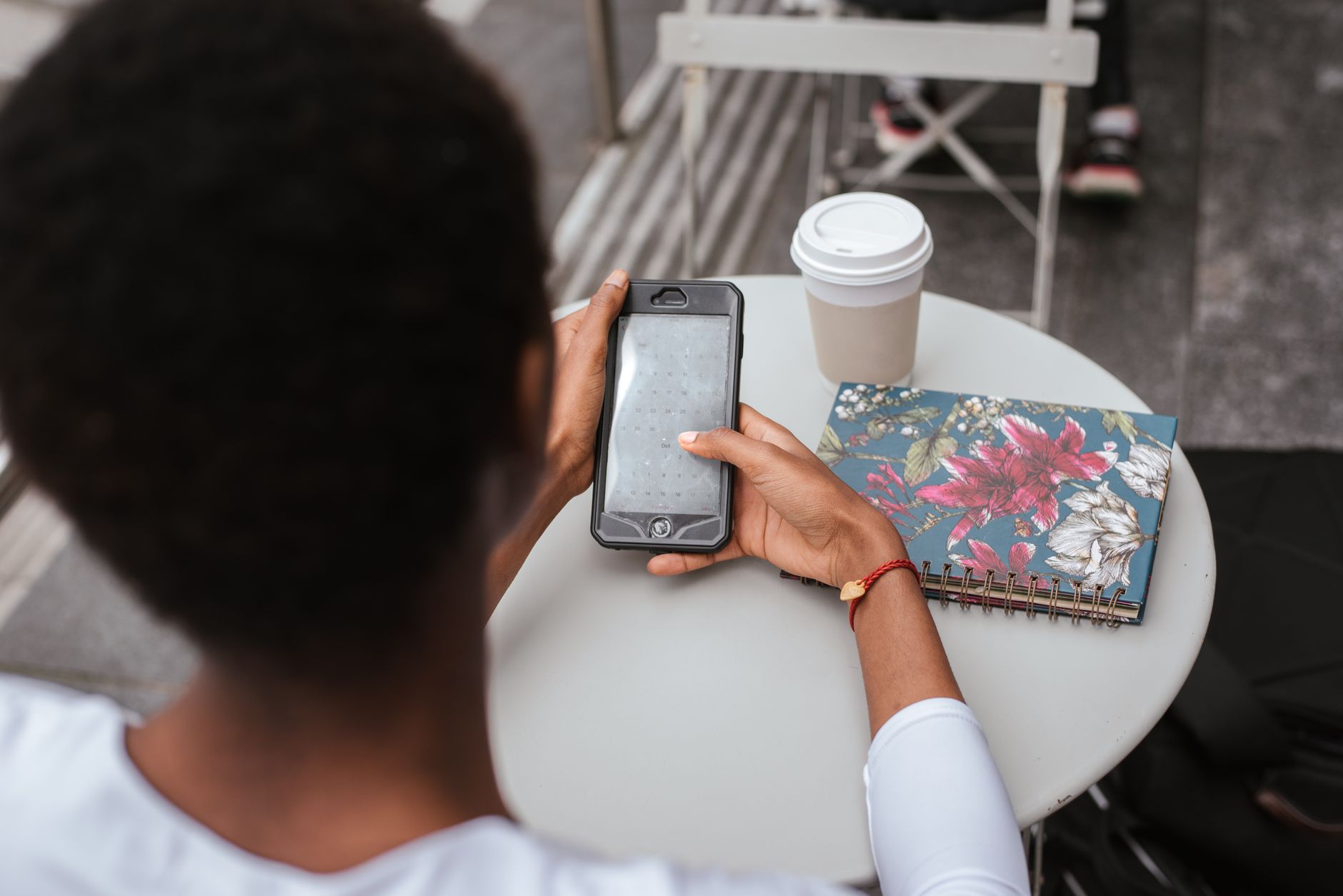 A medical traveler in Türkiye checks her phone at a cafe table with coffee and a floral notebook.