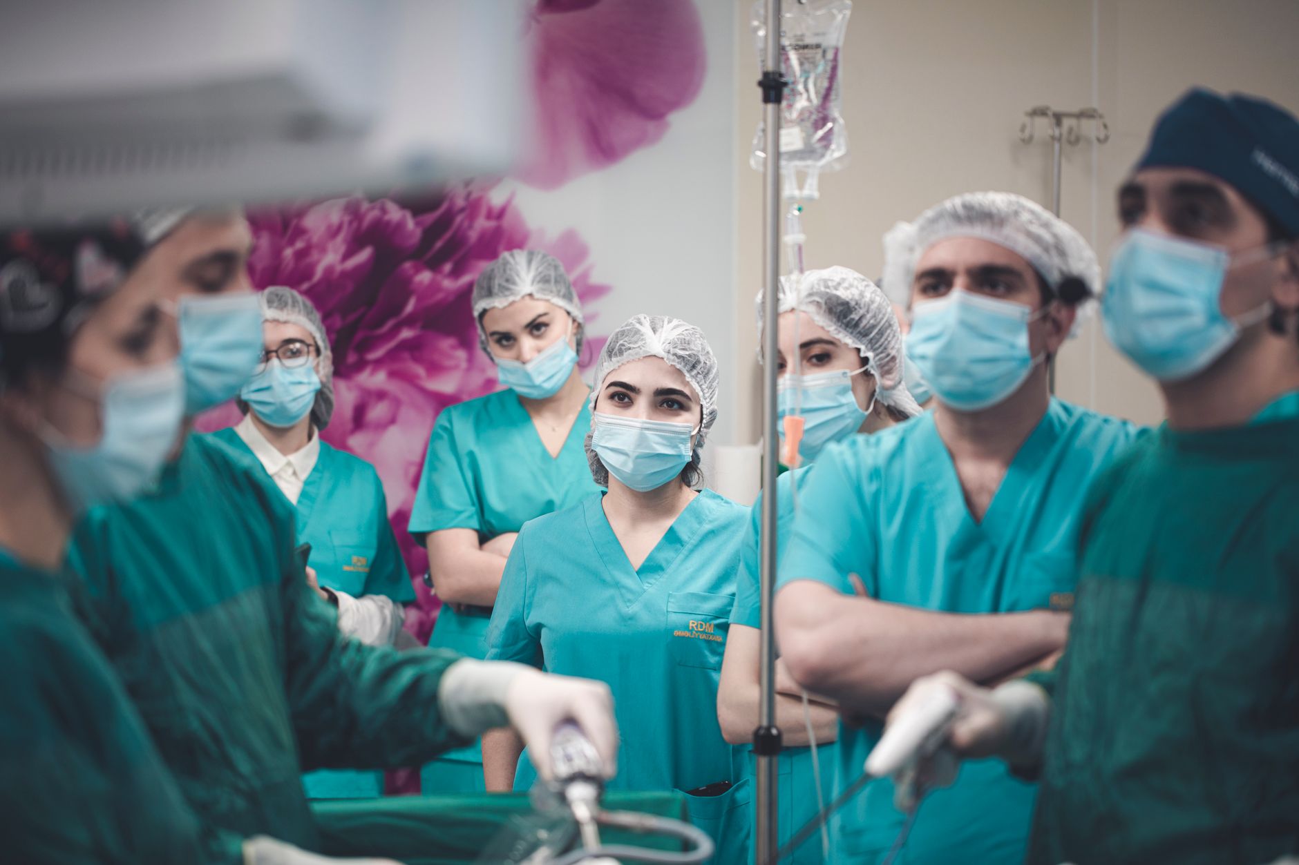 A team of surgeons in teal scrubs and masks observing a laparoscopic procedure in a clinical setting.