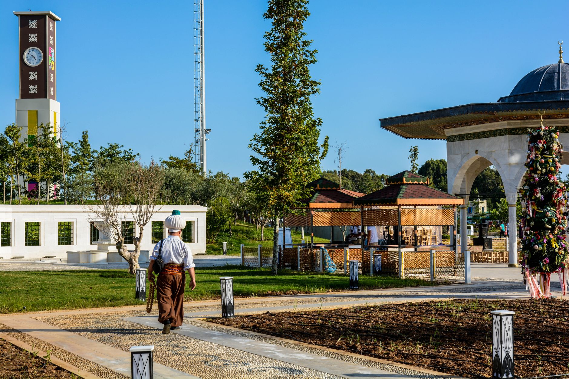 A man walks through a serene park in Antalya with green landscapes and traditional pavilions.