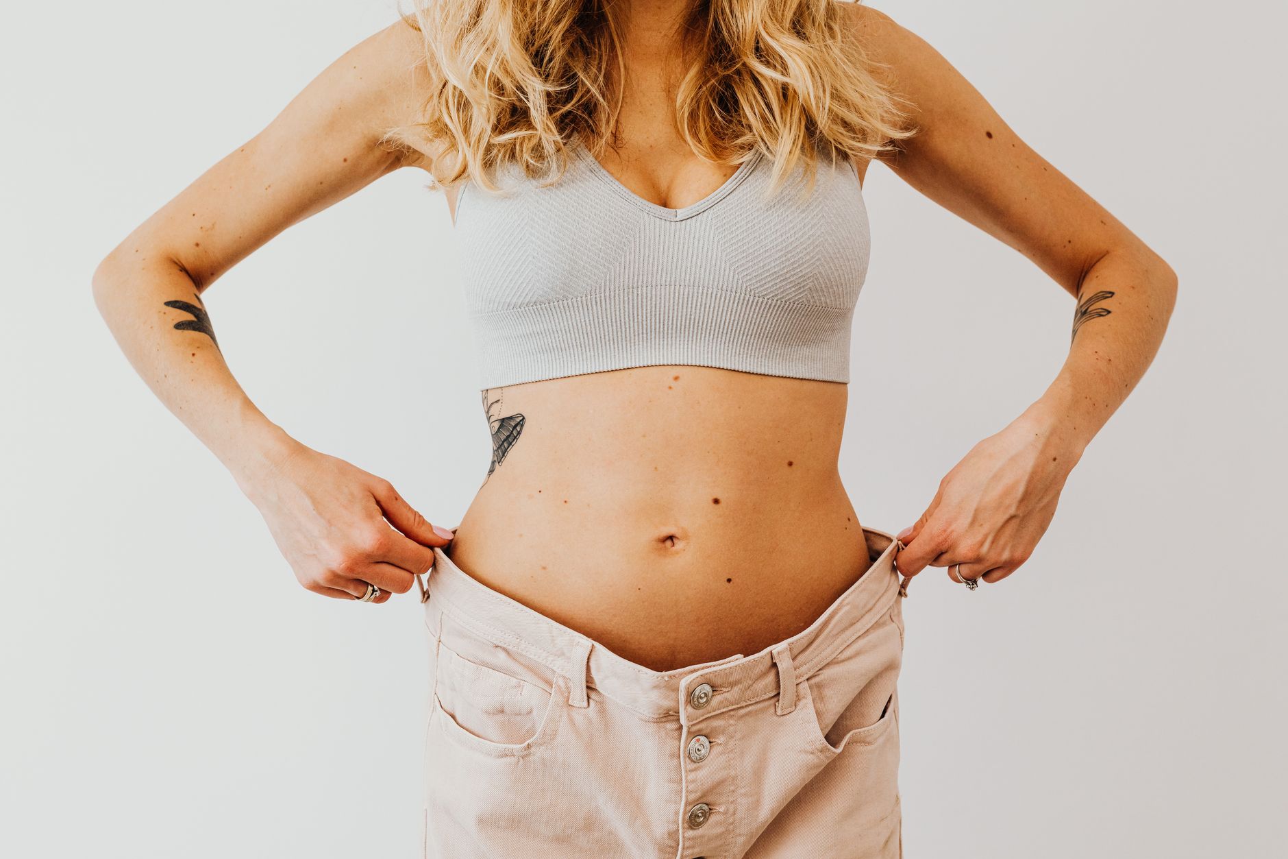 A smiling woman showcases her new figure, holding baggy pants after weight loss.