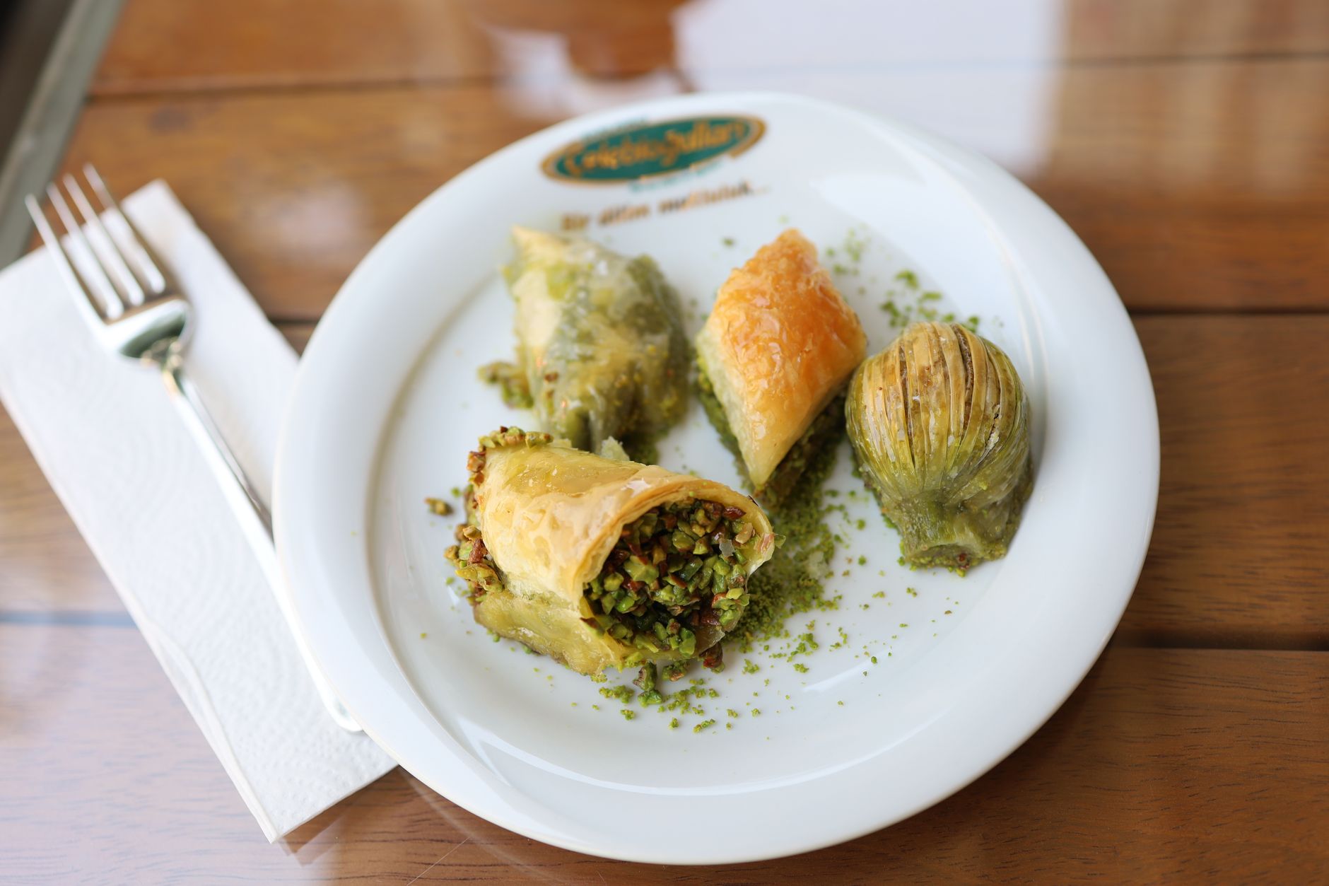 Bir tabakta fıstıkla süslenmiş çeşitli baklava dilimleri.