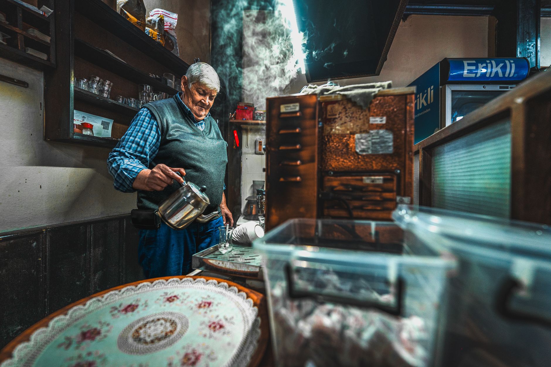 一位老人在温馨的约拉小屋里倒茶，水壶冒着热气。