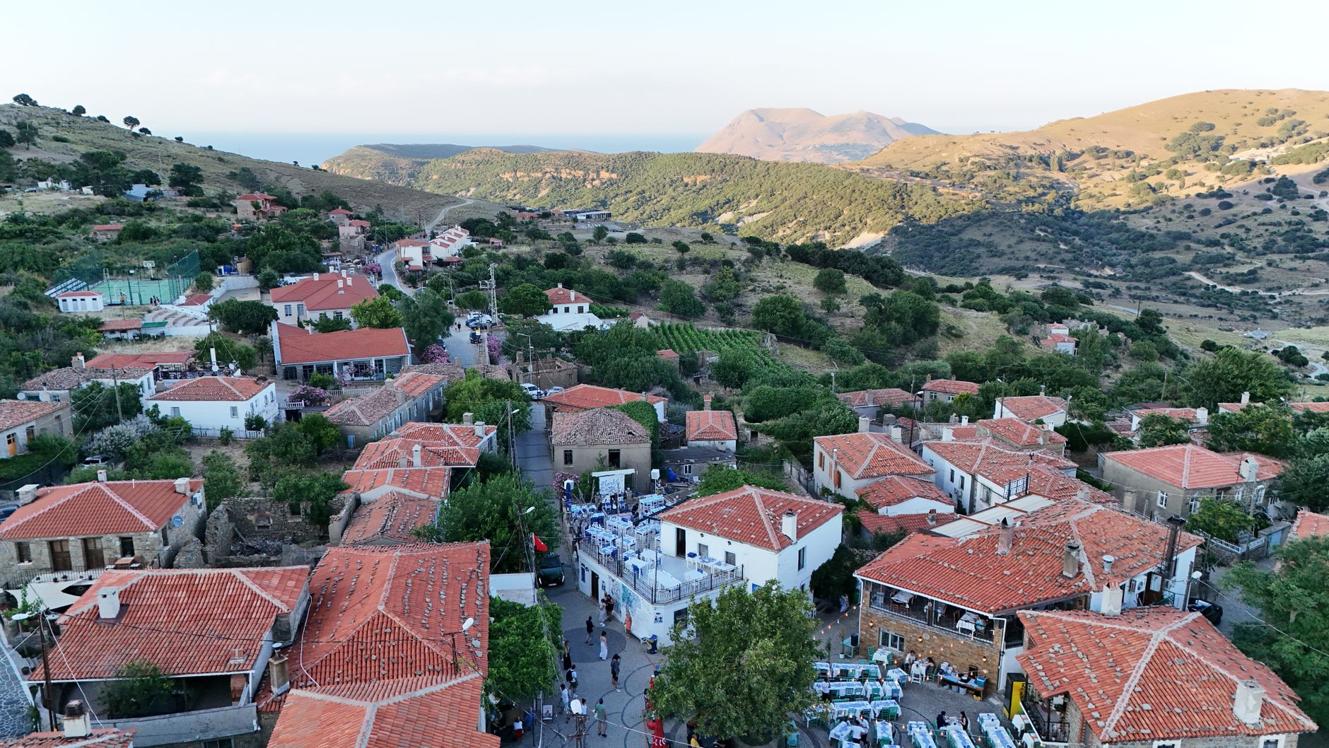 نمای هوایی از روستای دره‌کوی با خانه‌های سنگی سنتی و سقف‌های قرمز در میان تپه‌های سرسبز.