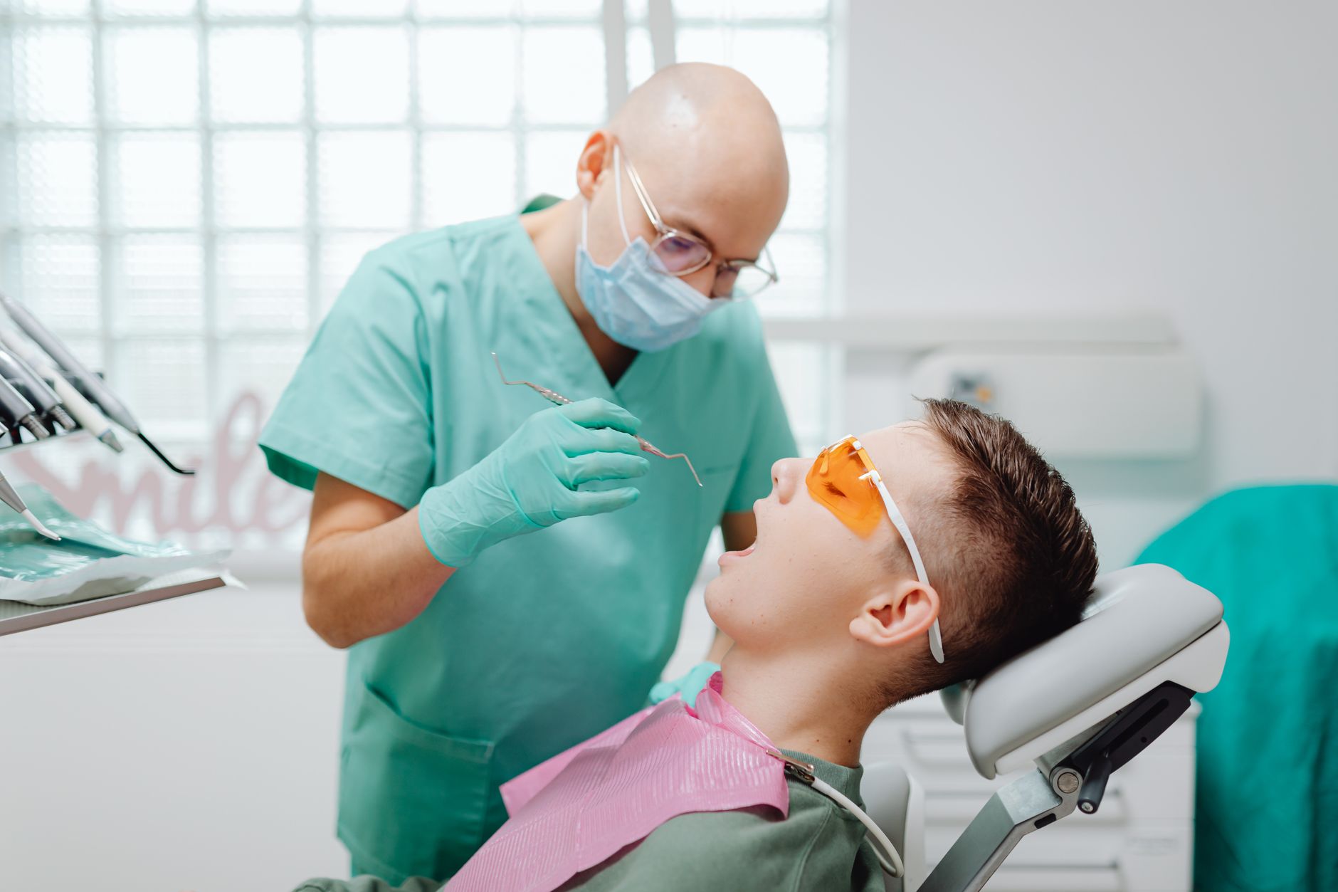 A dentist in a green uniform examines a patient's gums in a modern dental office.