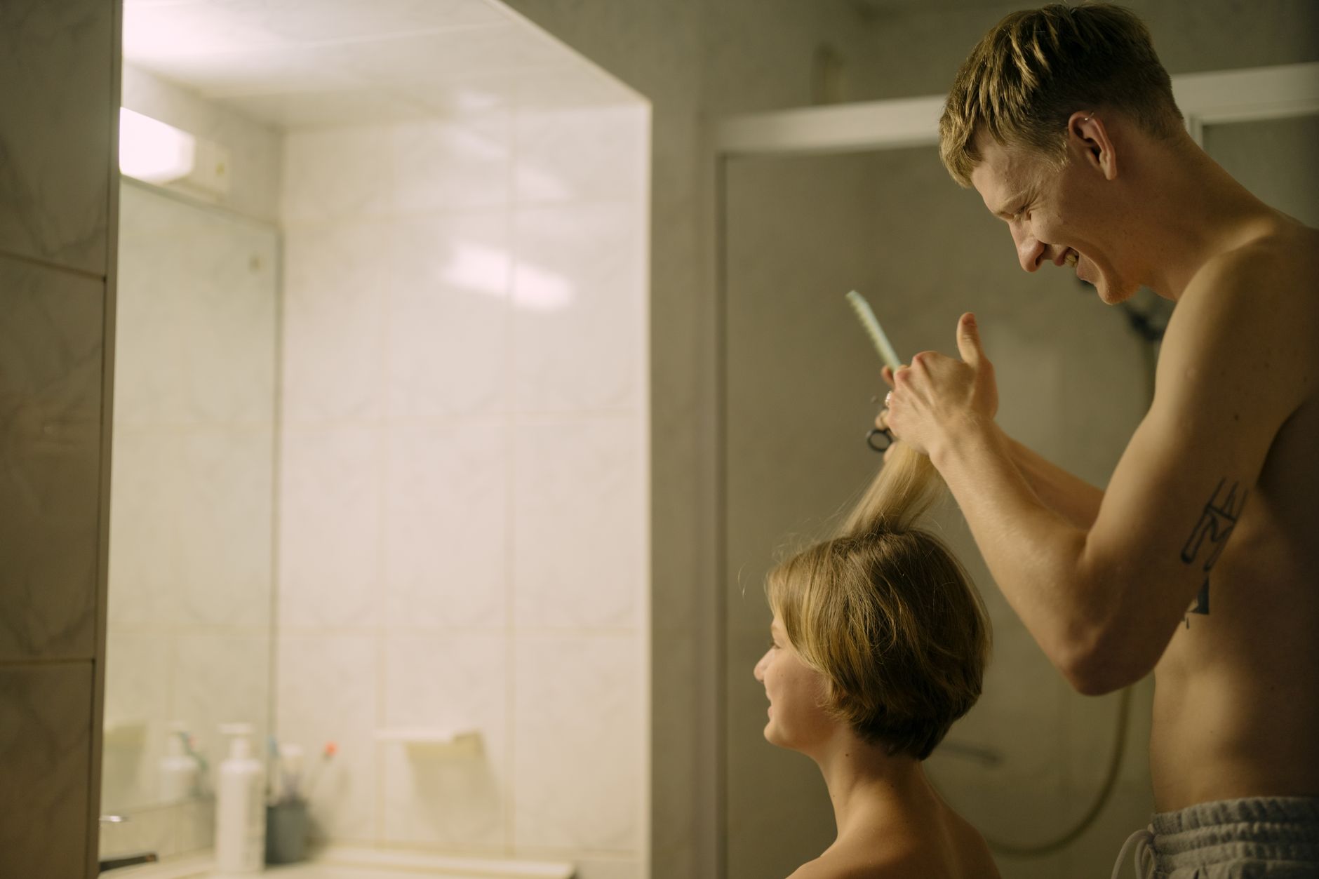 A man joyfully cuts a woman's hair in a bathroom, showcasing a casual and intimate moment.