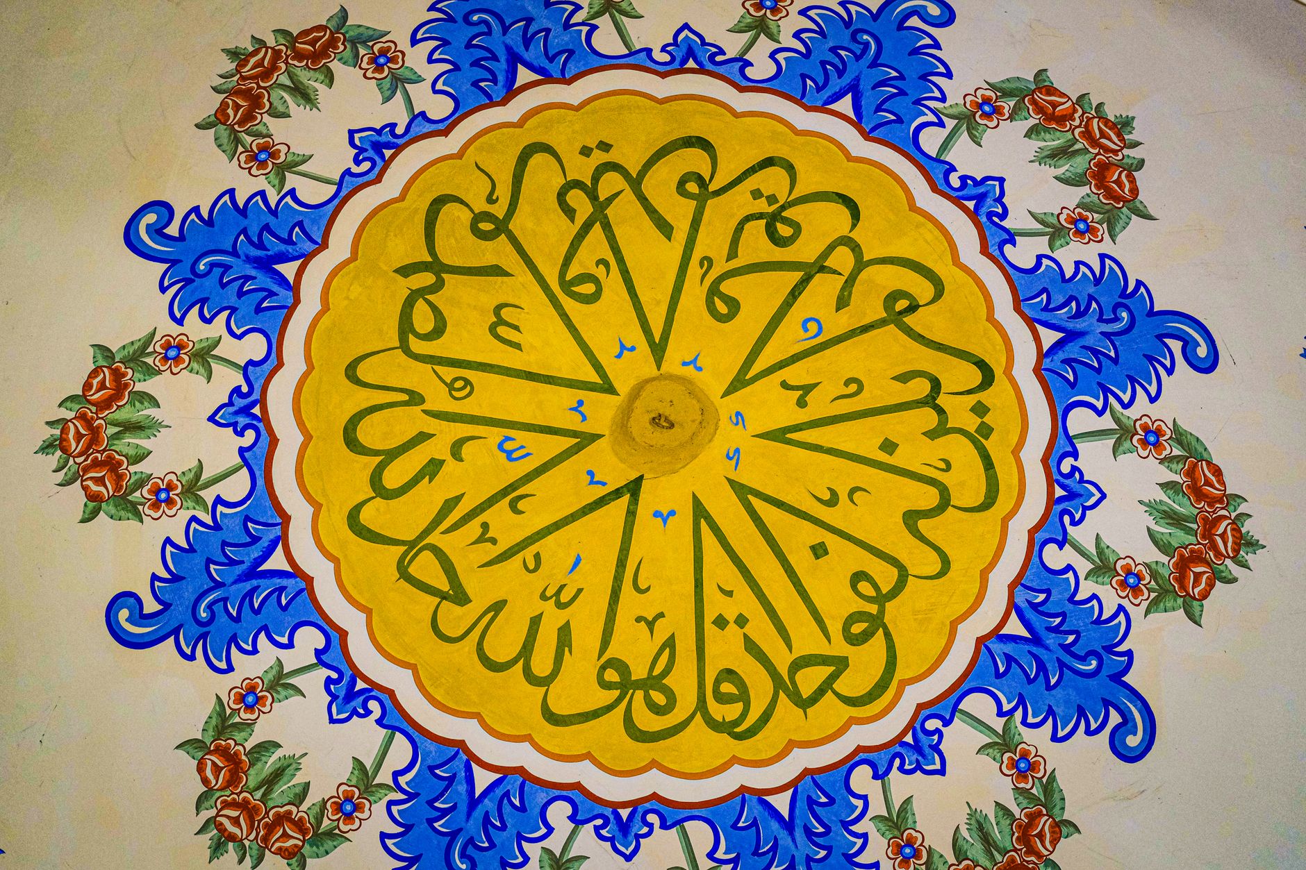 منظر قريب لزخارف زهرية ملونة مرسومة يدويًا وخط عربي على جدار مسجد.