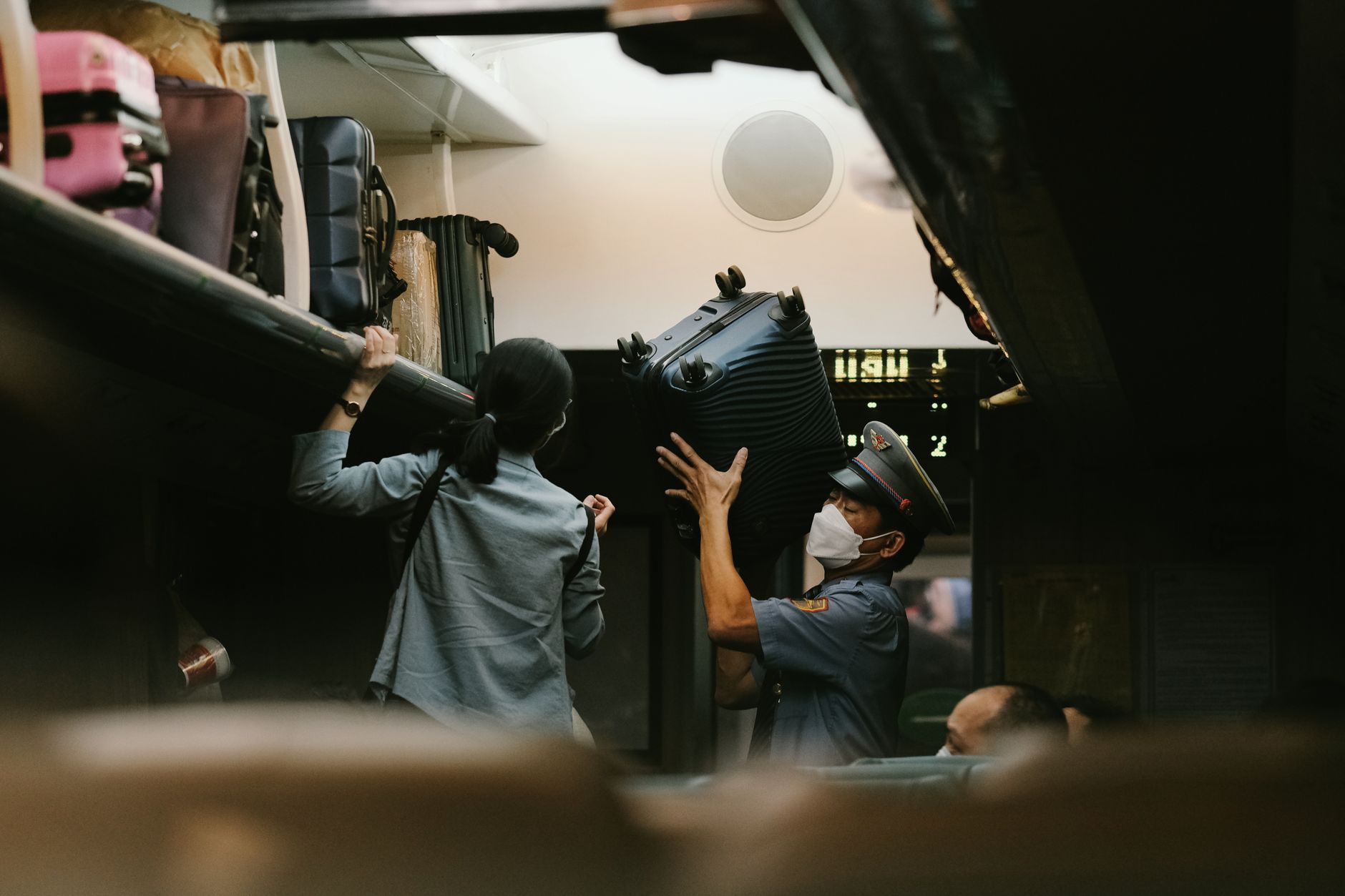 A train staff member helps a passenger with a suitcase on a train.
