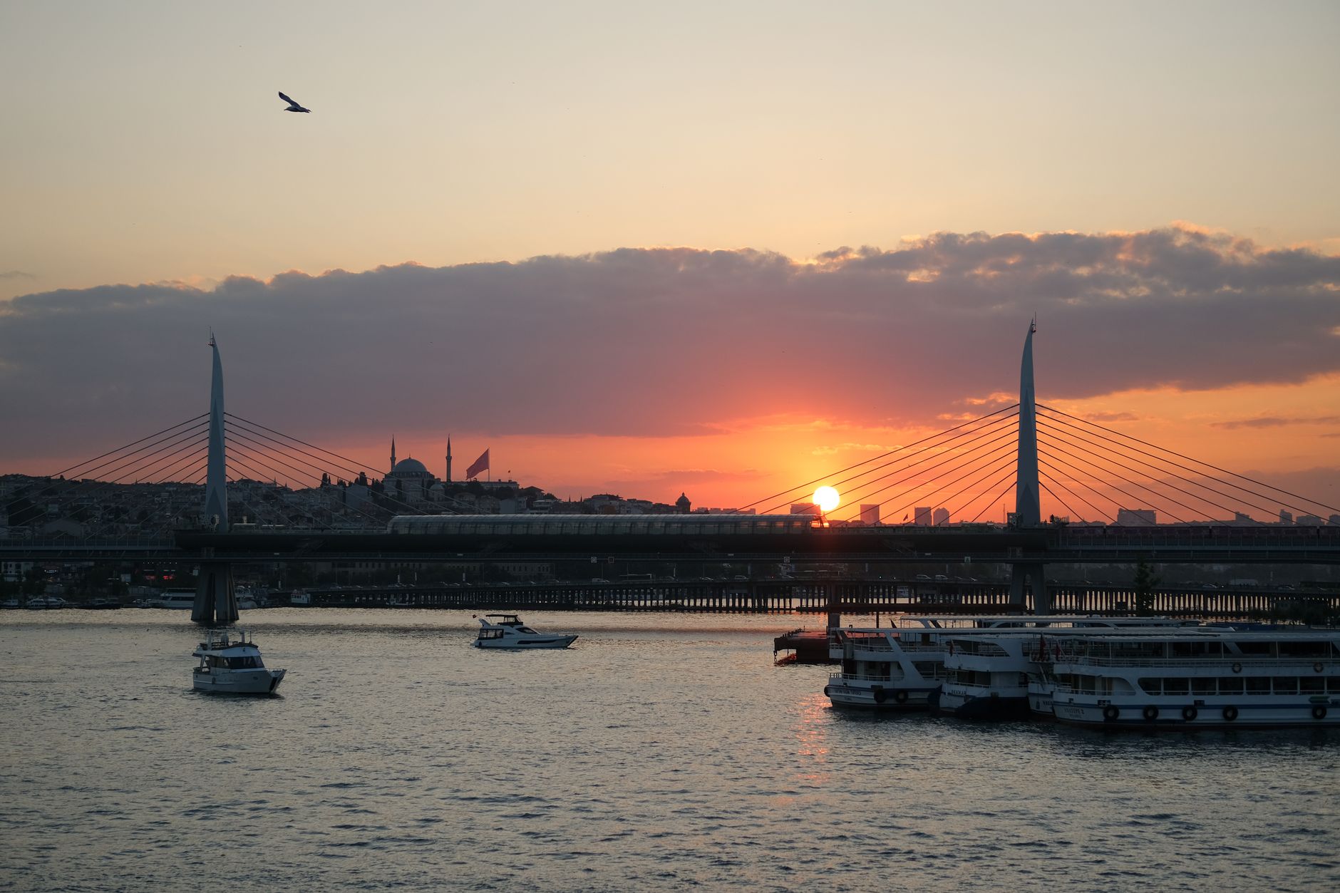 A picturesque sunset view over the Golden Horn, featuring boats and a bridge silhouette.