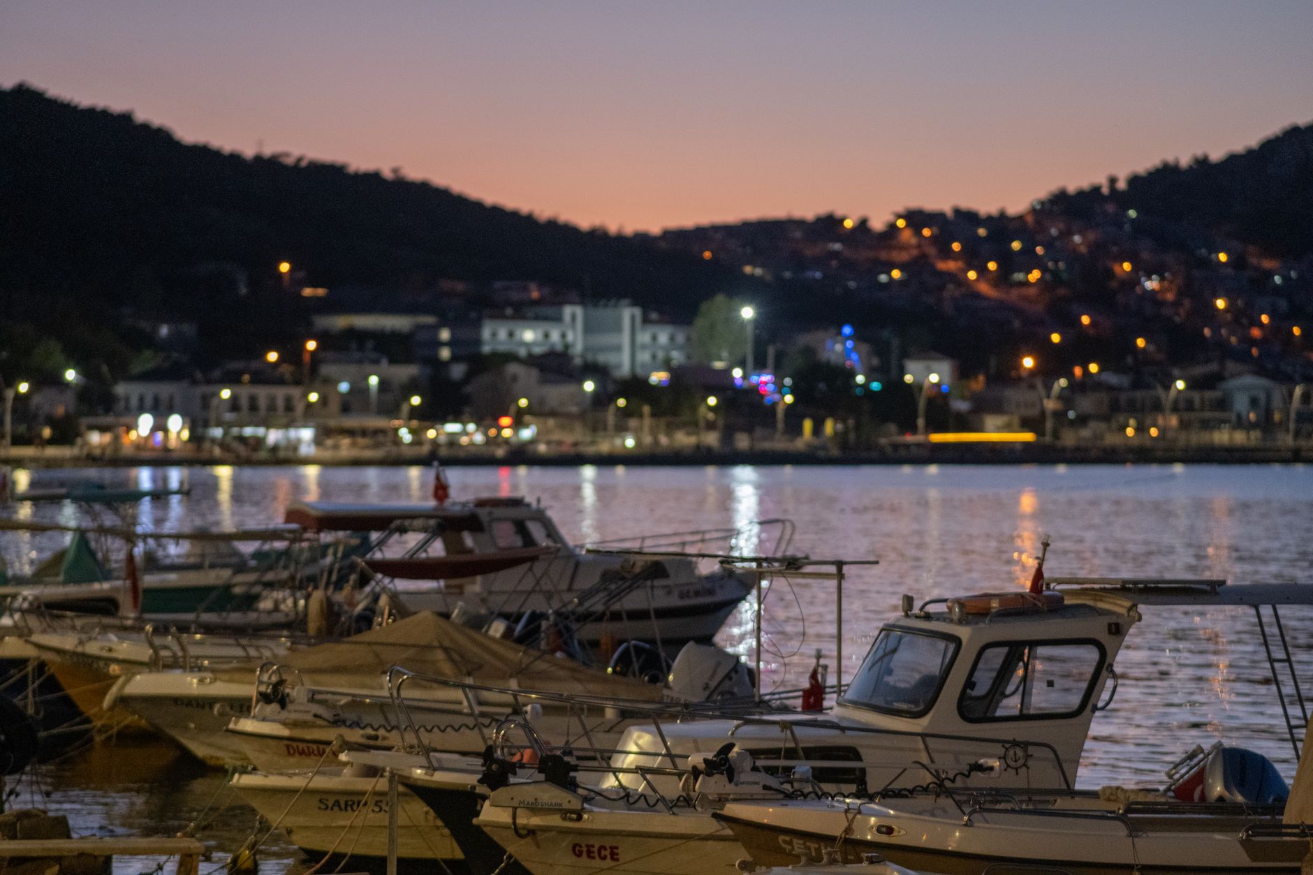 Scenic view of fishing boats in İnebolu harbour during sunset, lights twinkling in the background.