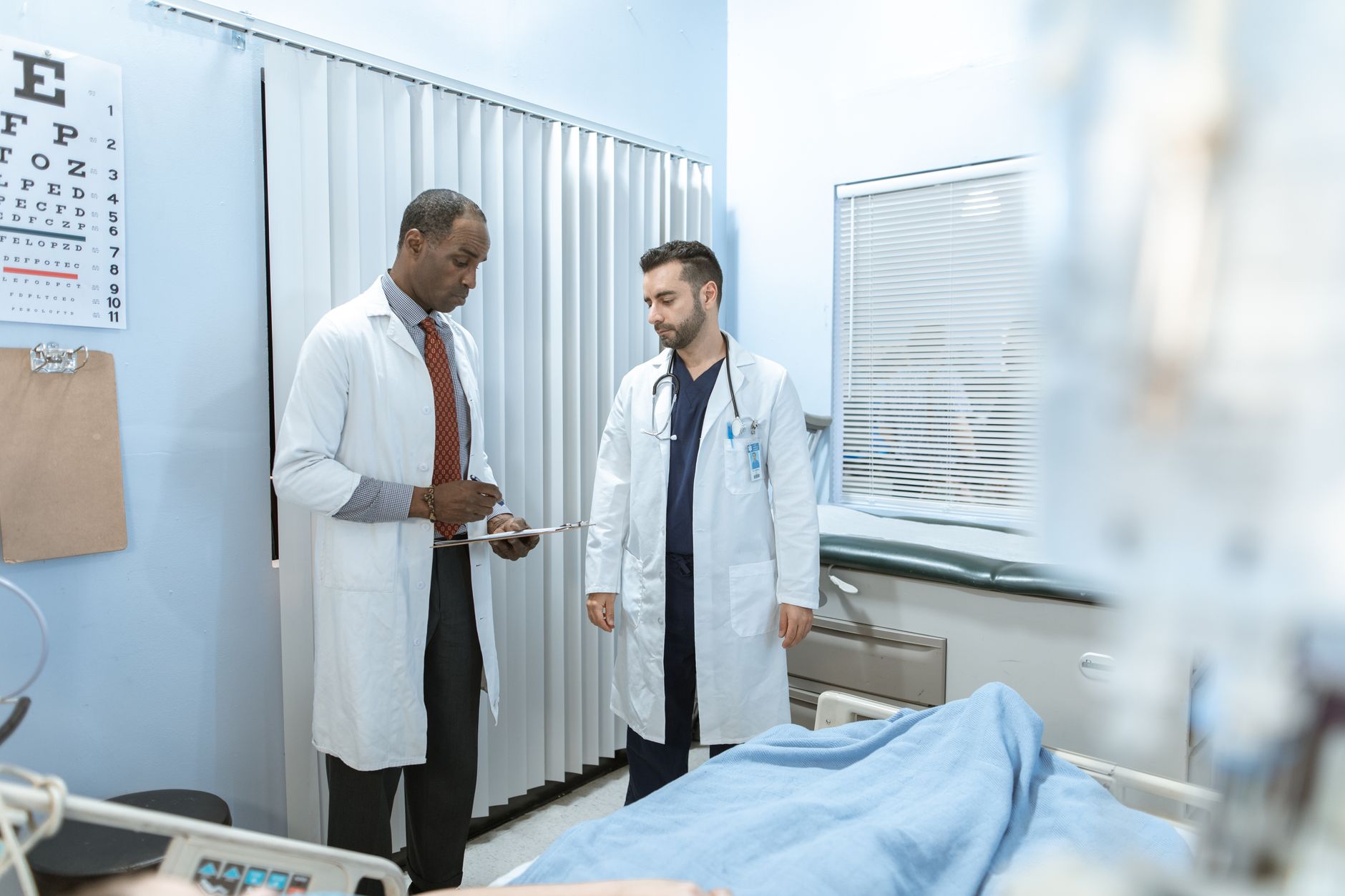 Two doctors in white coats reviewing a treatment plan in a hospital room.