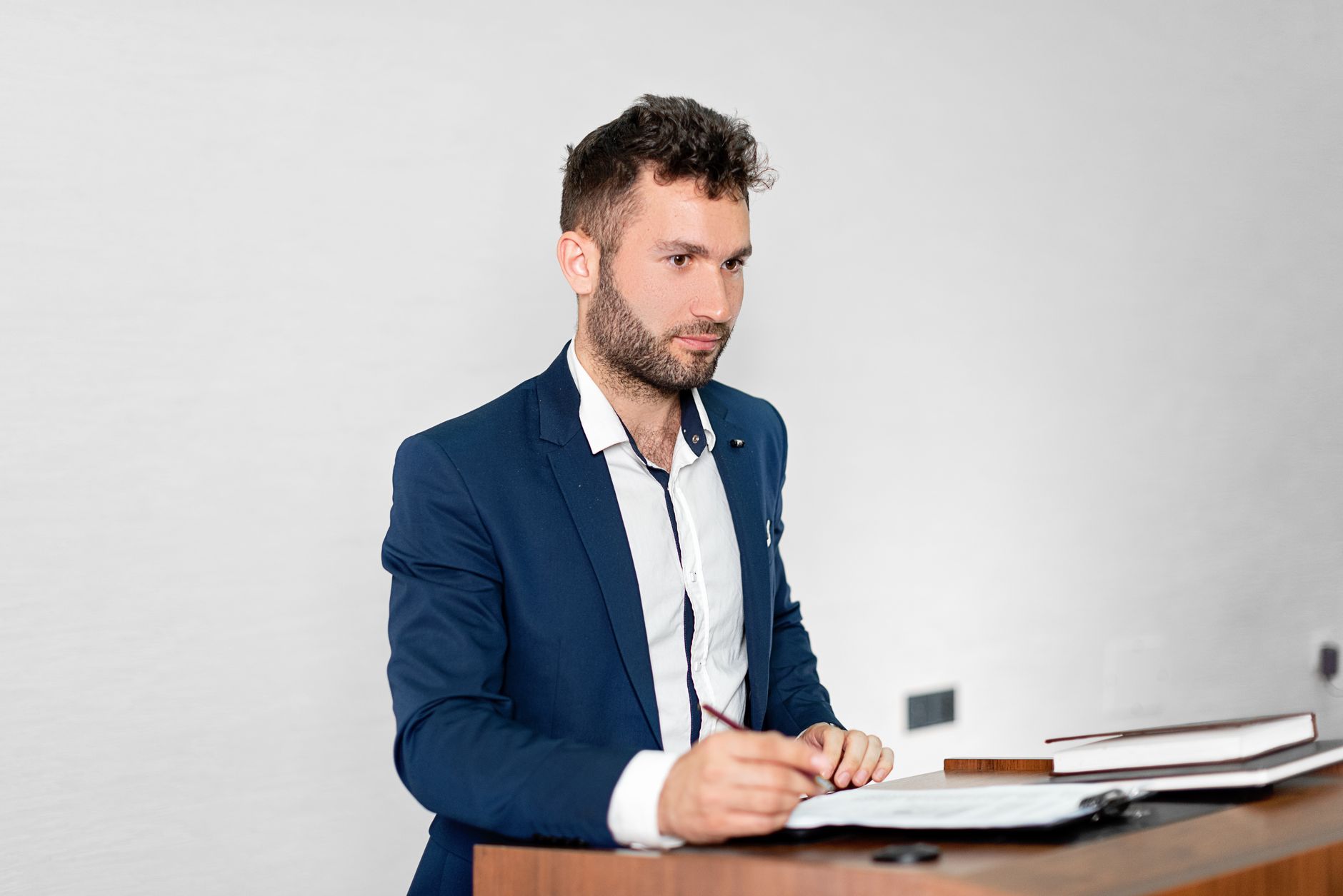 A clinician in a blue suit stands at a lectern, writing notes at a dental implantology congress.