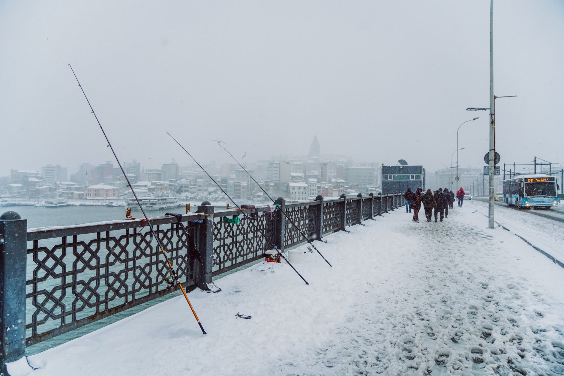 Snow-covered street in Istanbul with fishermen and pedestrians enjoying a winter day.
