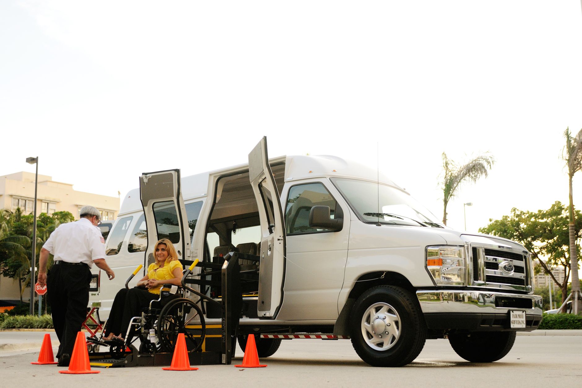 Airport staff helping a female passenger in a wheelchair board an accessible van.