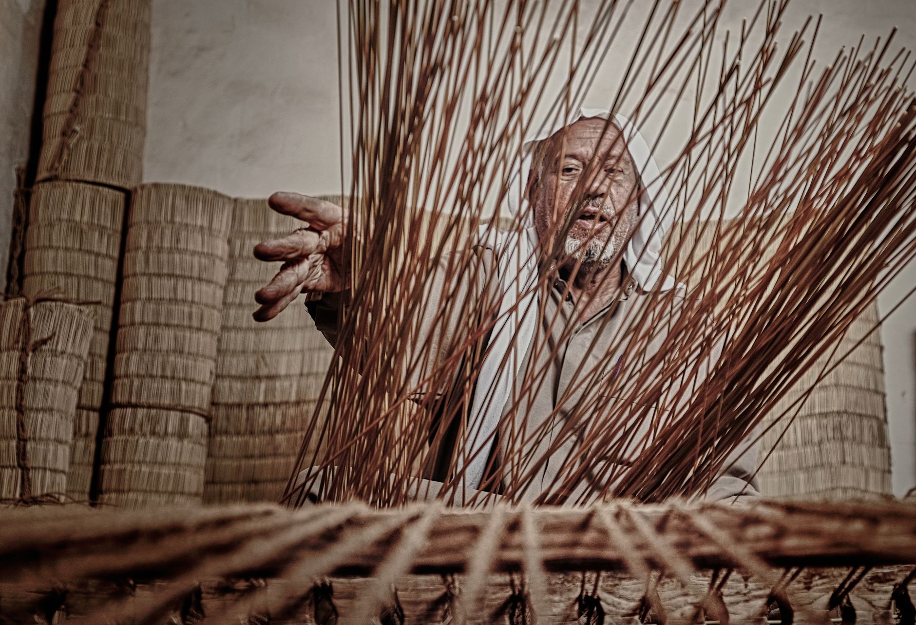 Yaşlı bir zanaatkârın rattan hasırı beceriyle sandalye iskeletine örmesi.