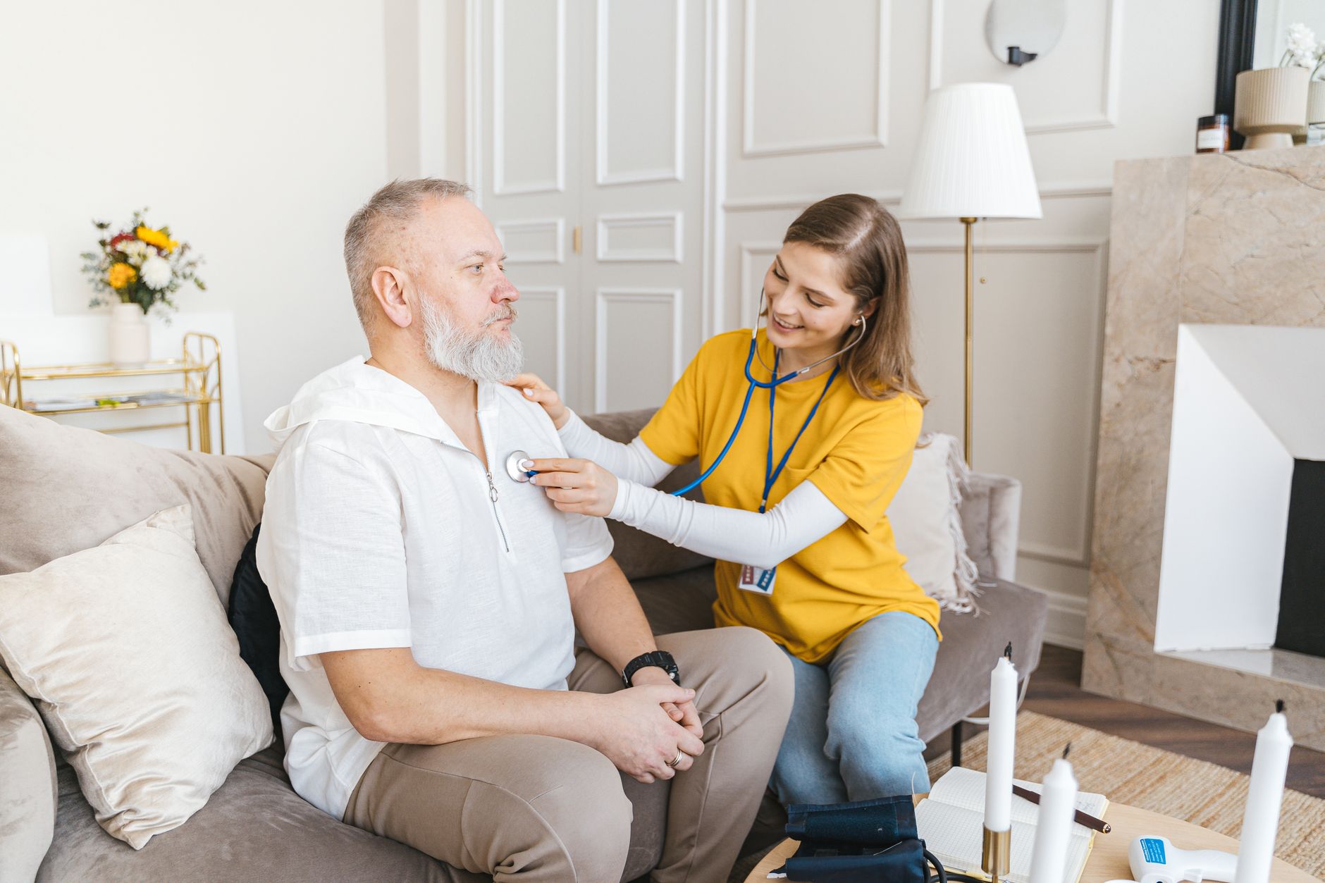 A nurse uses a stethoscope to examine a patient during a home visit.