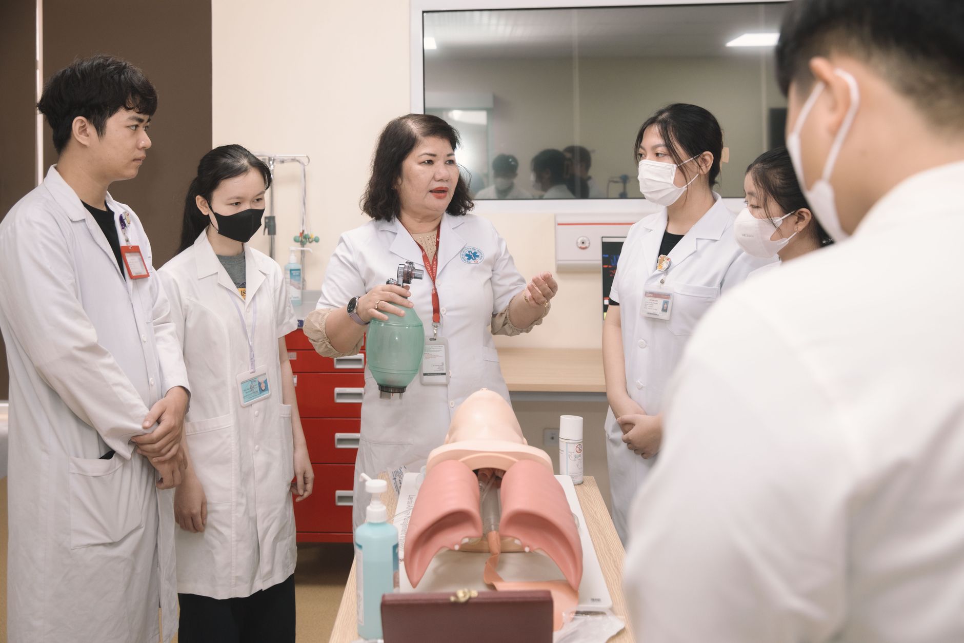 A nurse instructs trainees on medical equipment in a classroom.