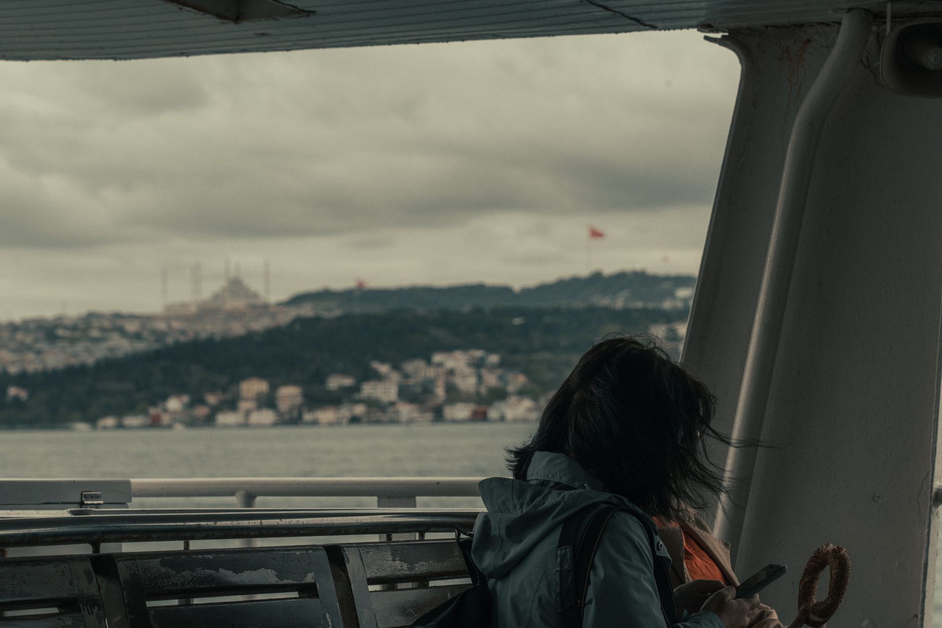 A woman on a ferry in Istanbul, gazing at the city while using her phone.