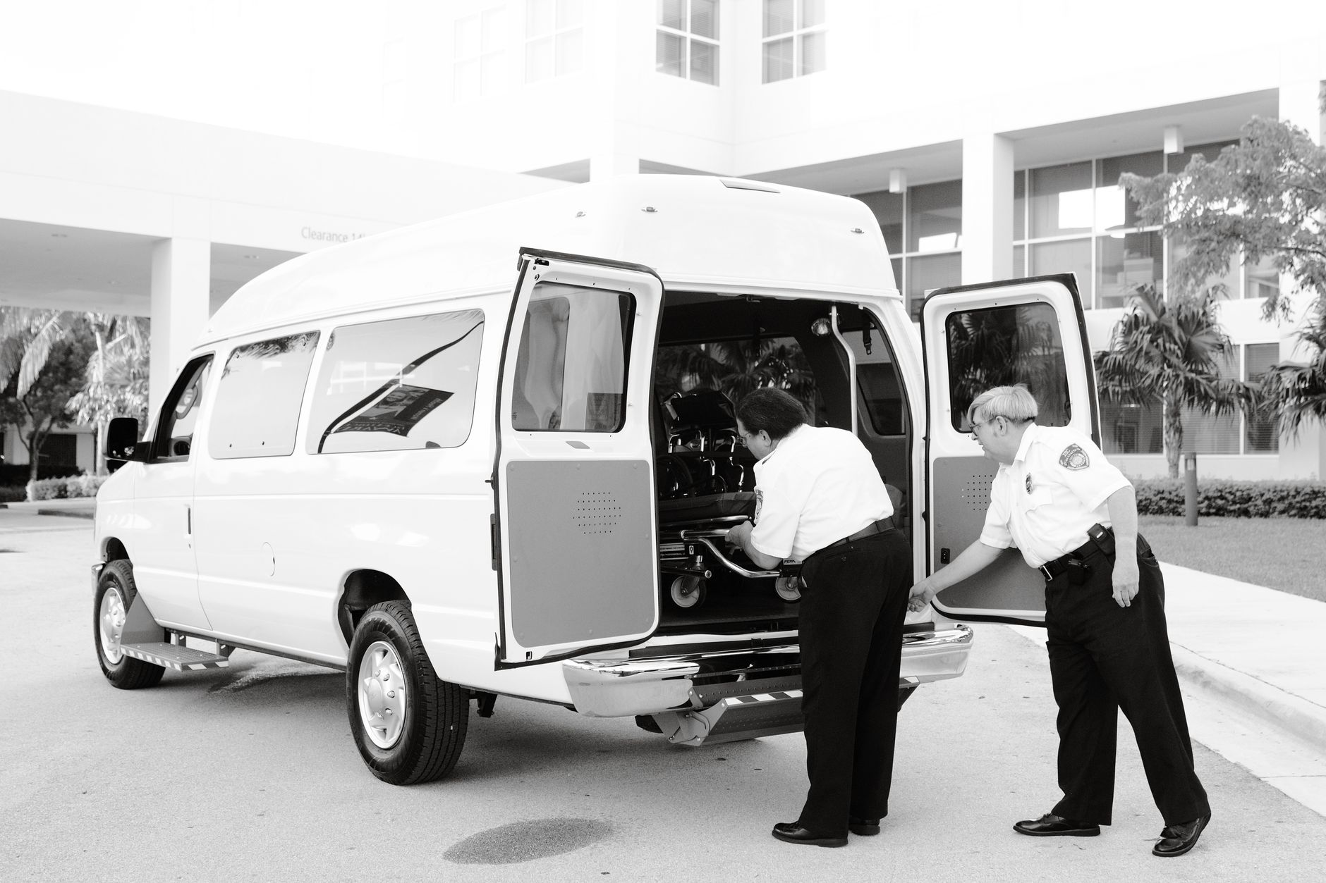 Two individuals preparing a stretcher from a medical transfer vehicle outside an airport terminal.