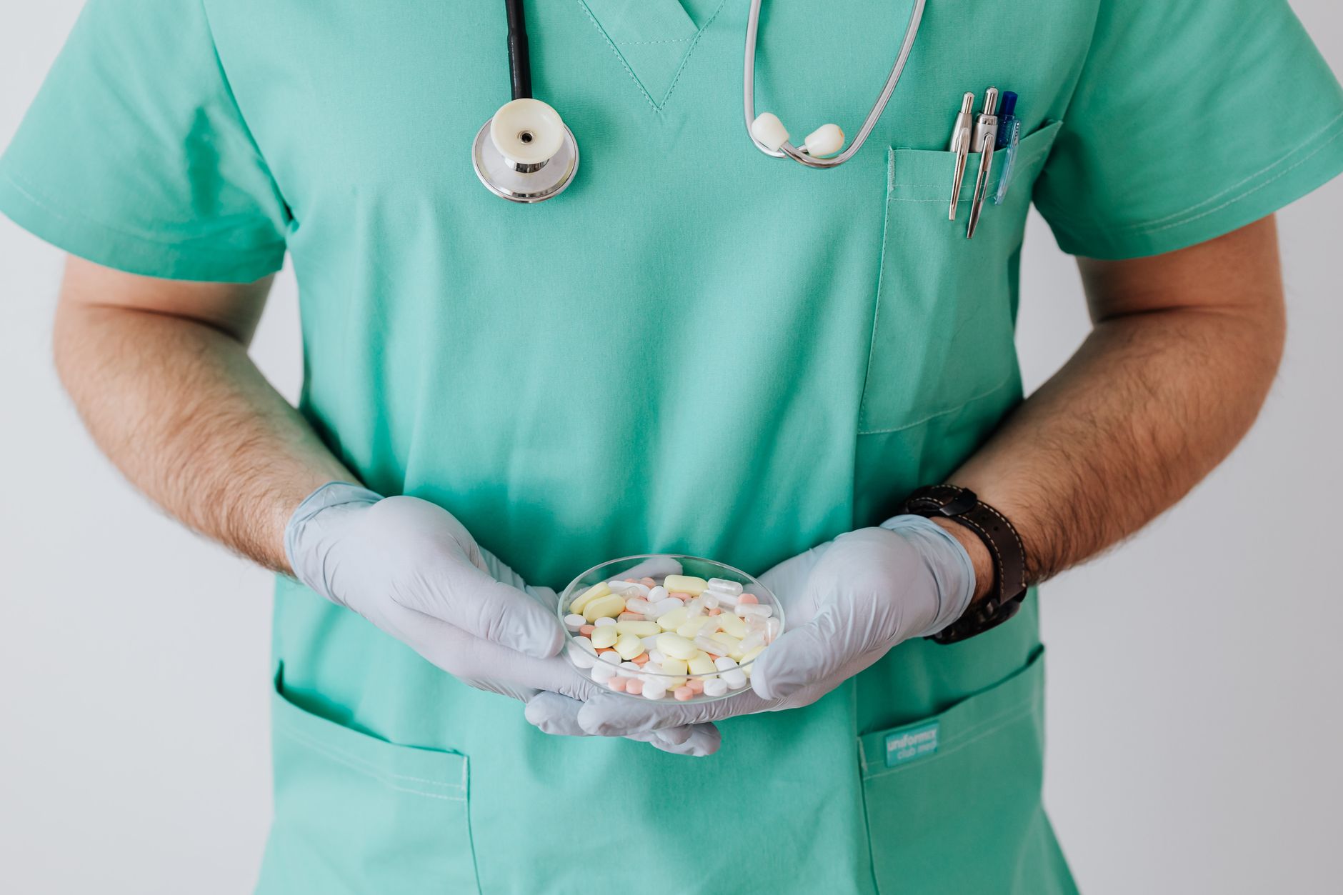 A healthcare professional in green scrubs holding a dish of assorted pills.