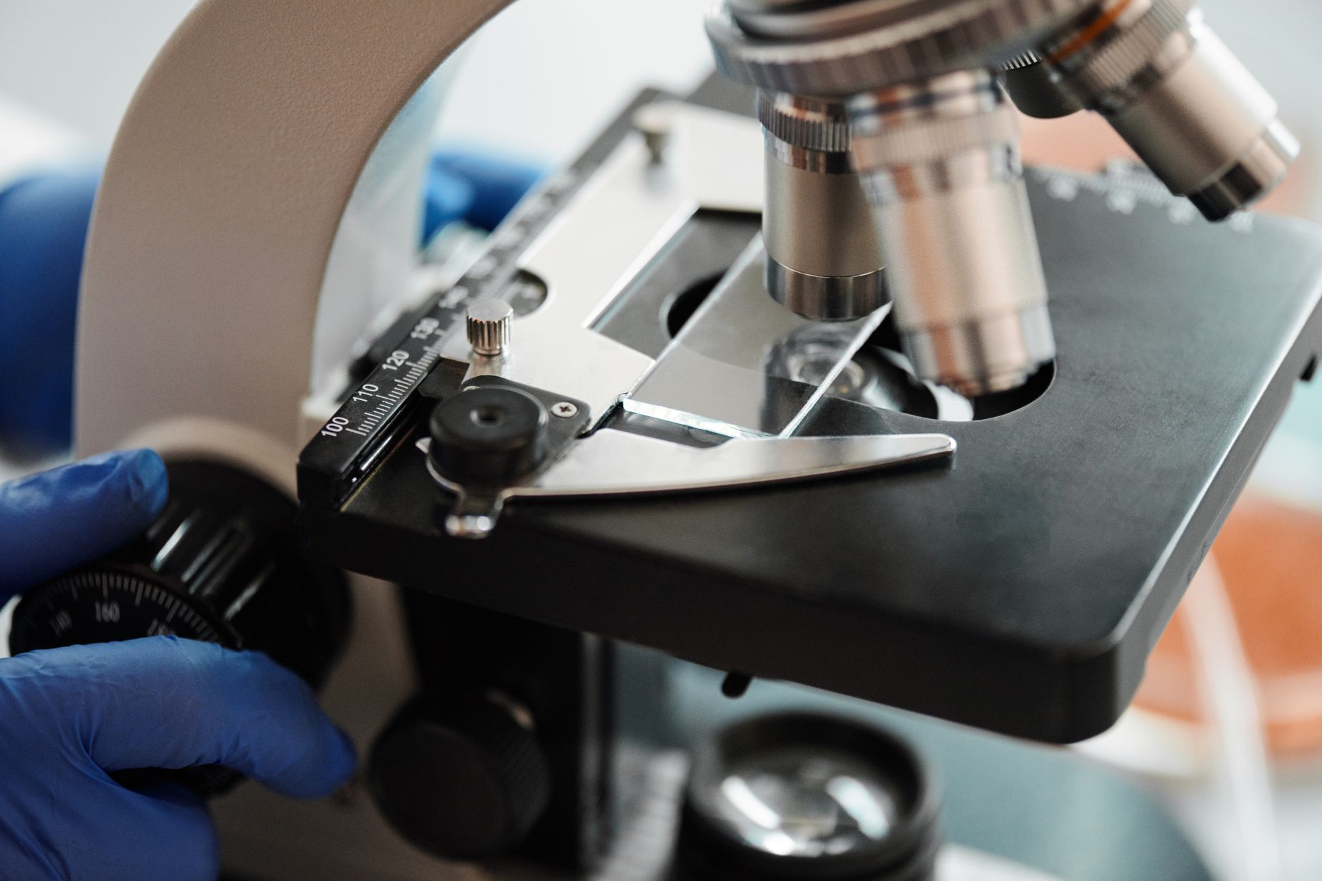 Close-up of a microscope with a gloved hand adjusting focus in a hospital lab.
