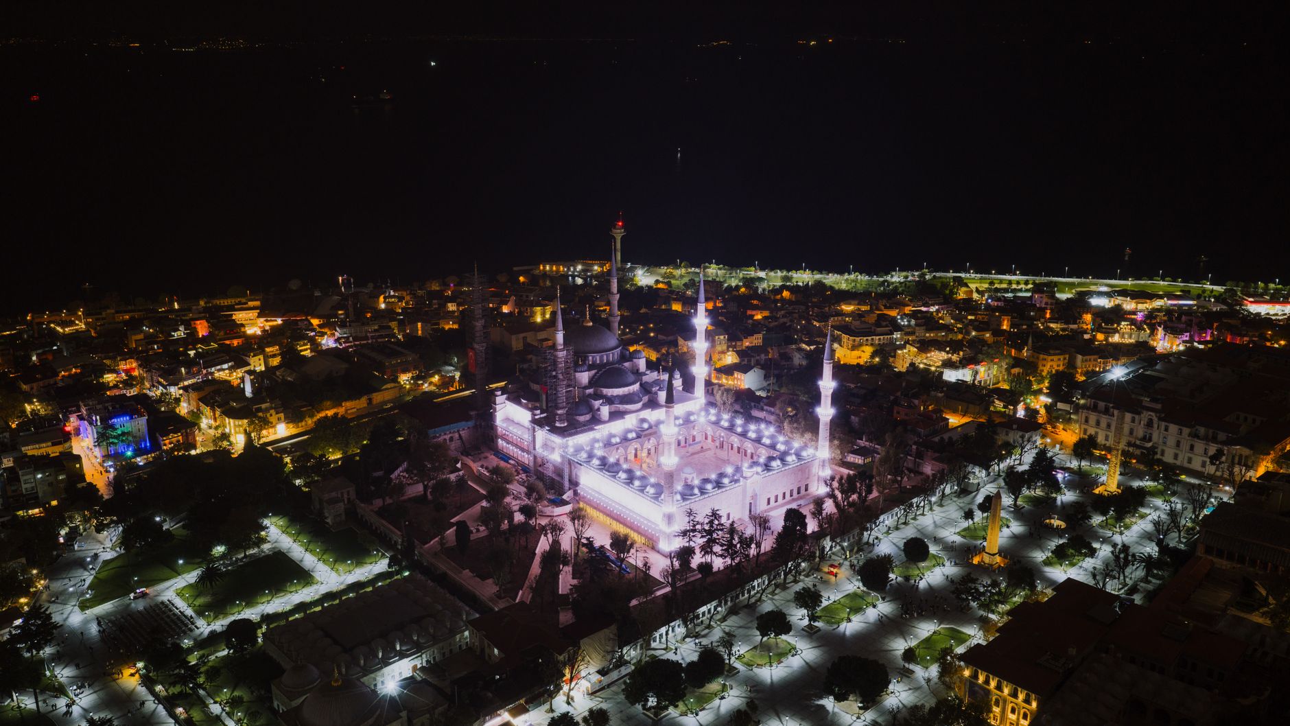 منظر جوي لساحة السلطان أحمد في إسطنبول، تُظهر المباني التاريخية وأضواء المدينة النابضة في الليل.