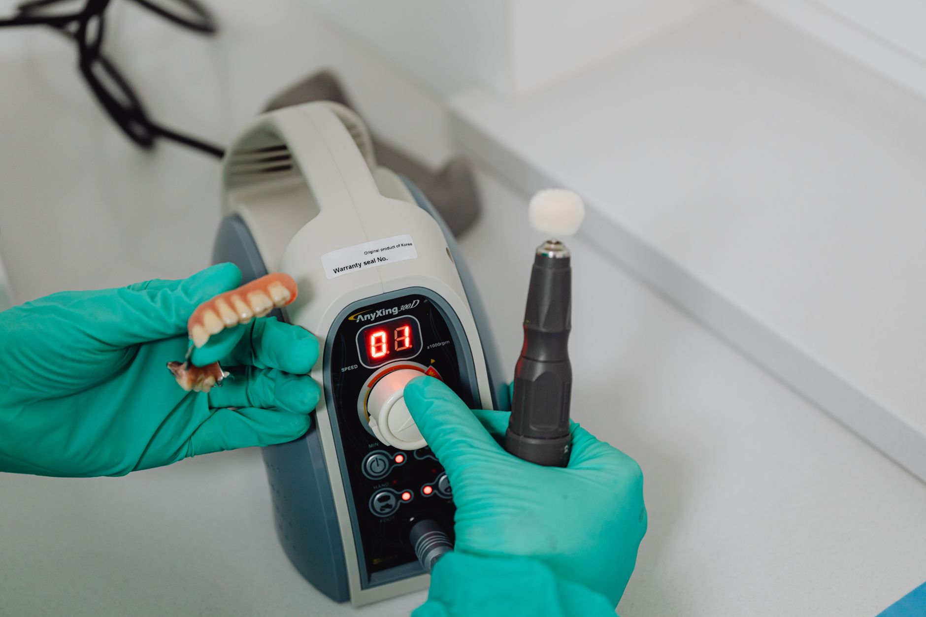 Technician in gloves operates a CAD/CAM milling machine with dental prosthetics.