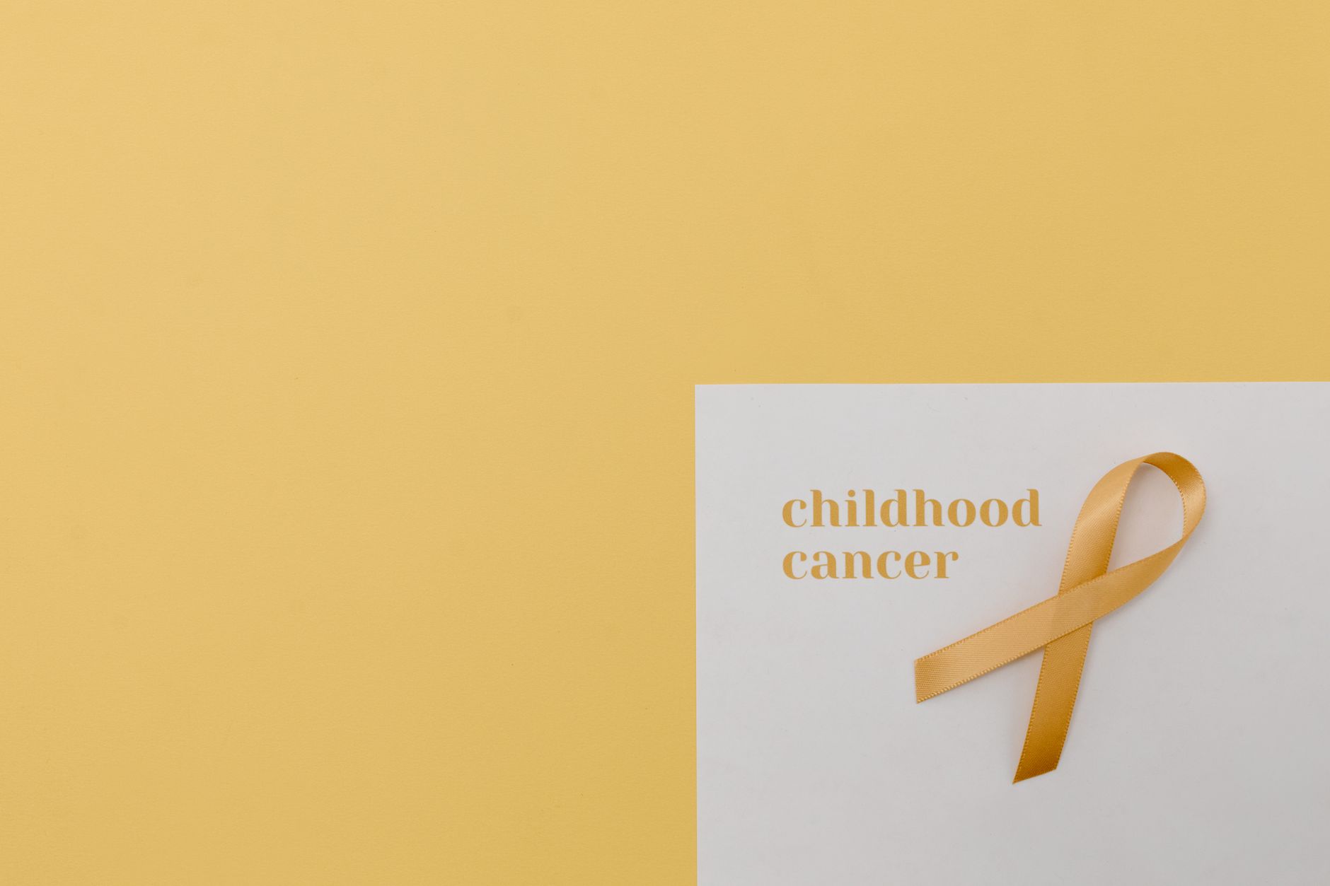 A yellow ribbon representing childhood cancer awareness on a white card against a soft yellow background.