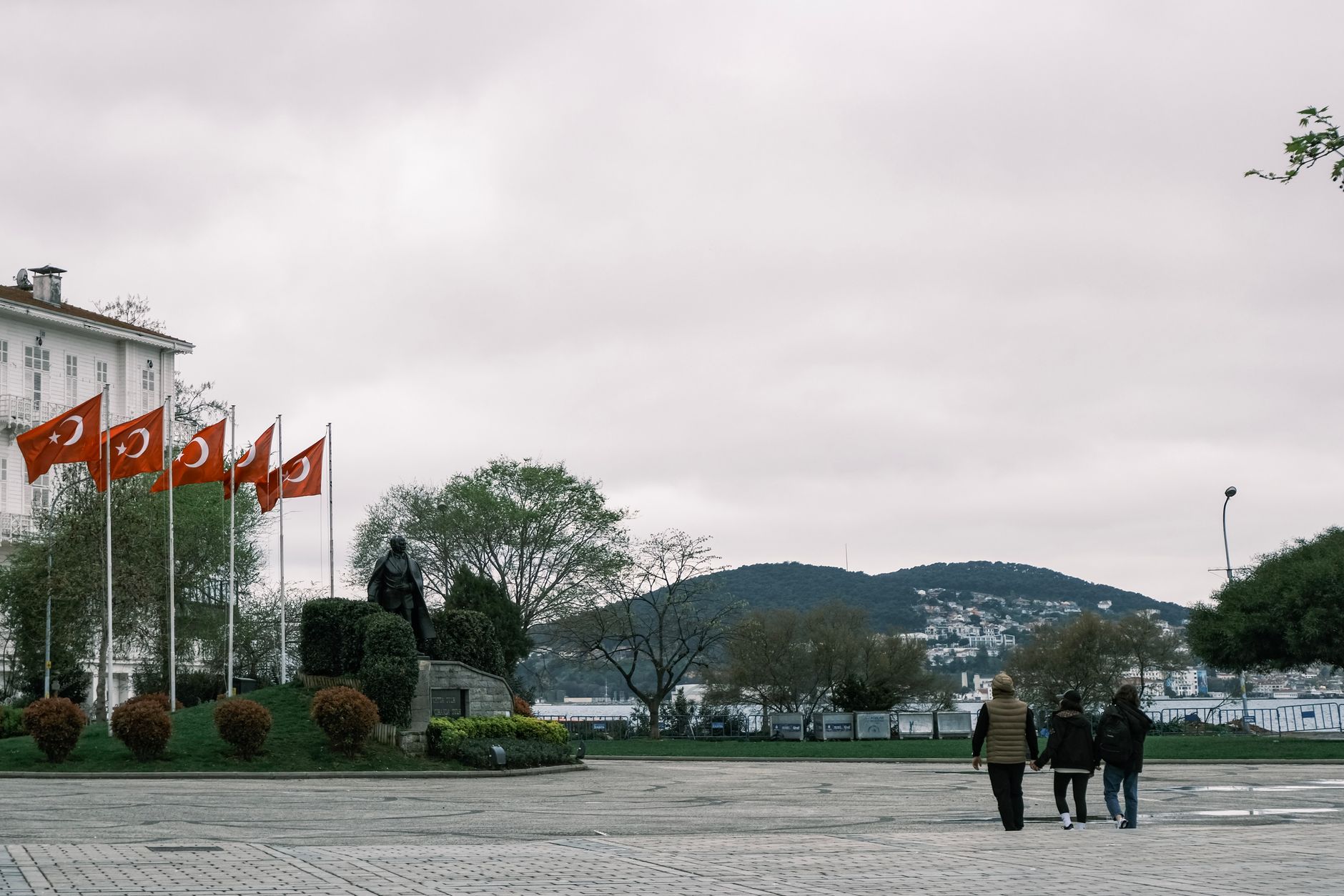 Recovered patient enjoying a walk by the Bosphorus with Turkish flags and a statue nearby.