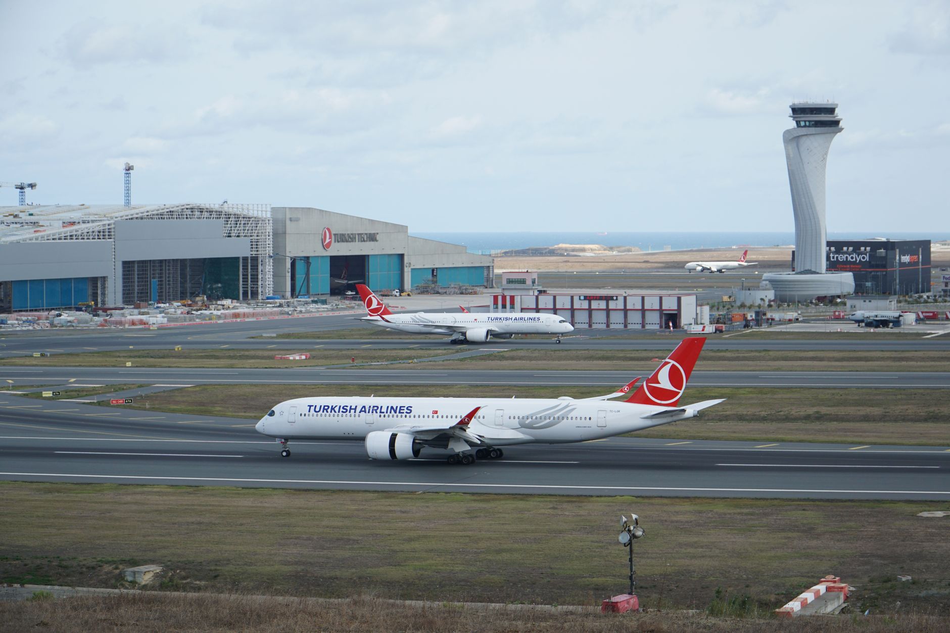 Two Turkish Airlines planes taxiing at Istanbul Airport with modern terminal in the background.