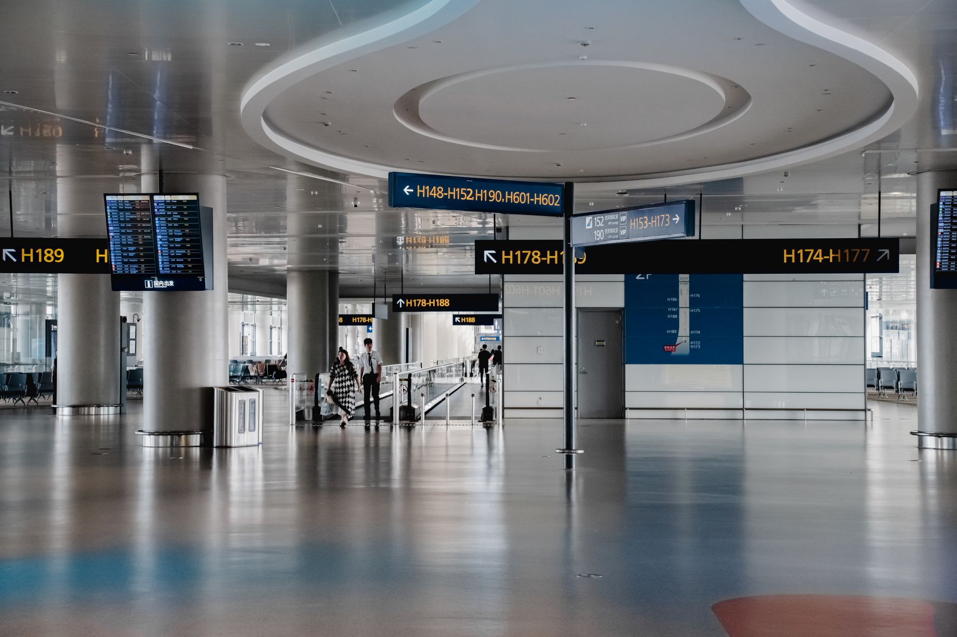 Spacious airport arrival hall featuring flight information boards and travelers navigating through the terminal.