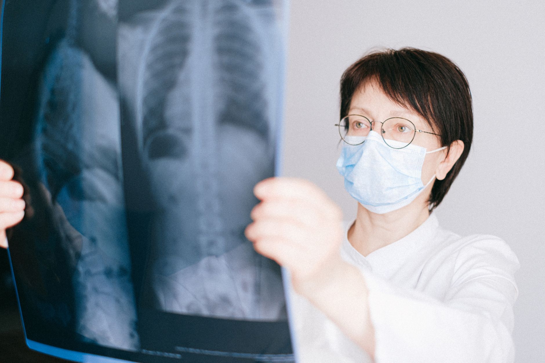 Medical professional in mask reviewing chest x-ray in a bright office.