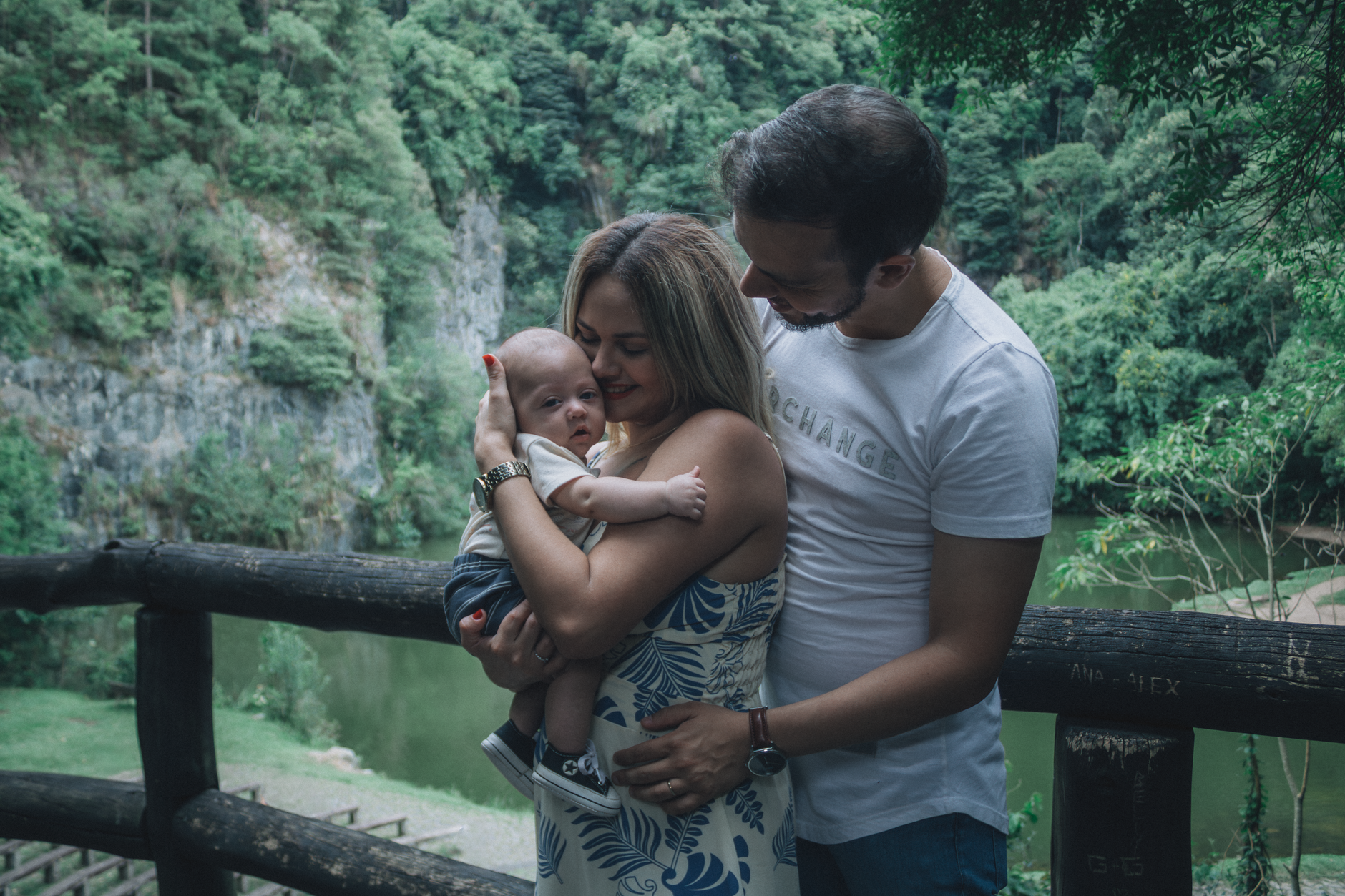 A happy couple embraces their baby in a lush green park, symbolizing family joy.