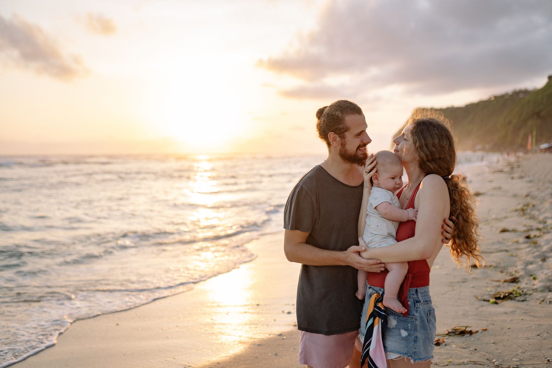 A happy couple at the beach holding their baby during sunset, symbolizing hope and new beginnings.
