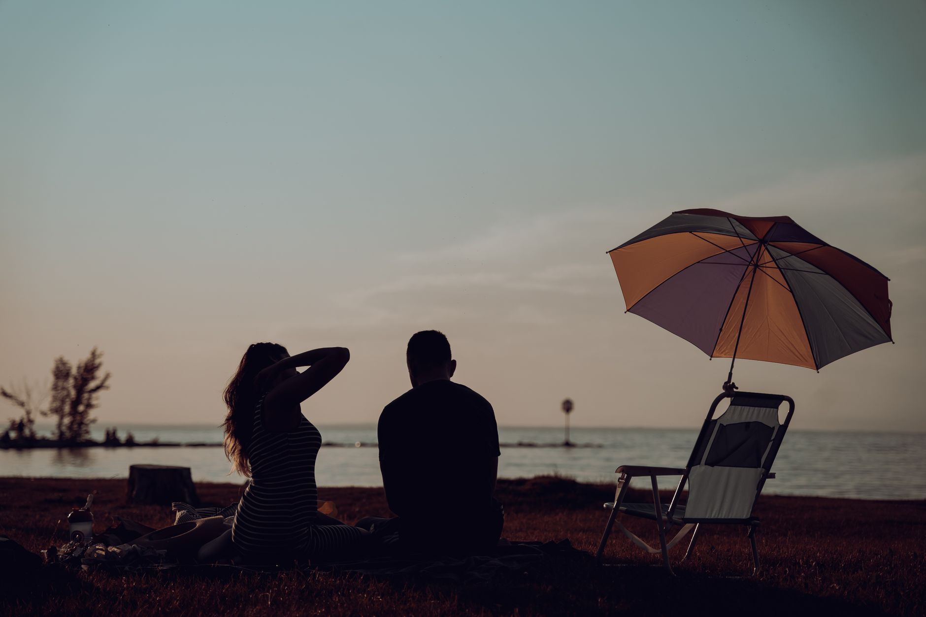 Silhouette of a couple sitting on the grass by the lake, enjoying a sunset.