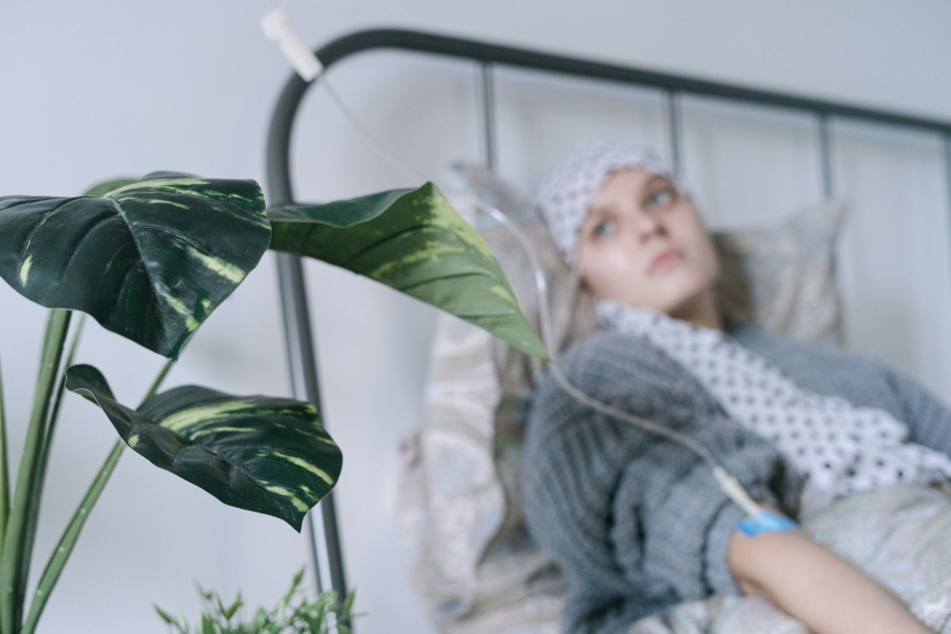 A patient with a headscarf lies in a hospital bed, receiving IV treatment.